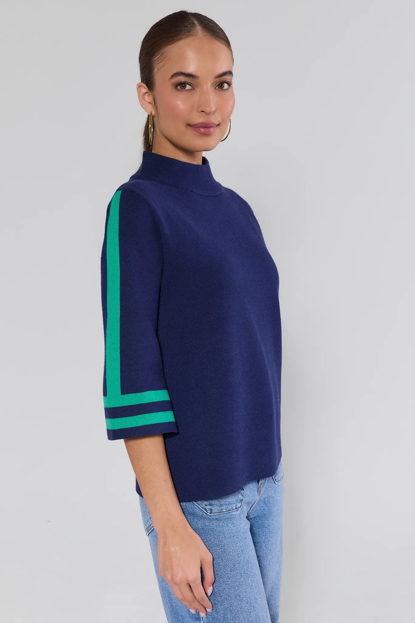 Woman wearing a navy jackie sweater with green accents on a plain background