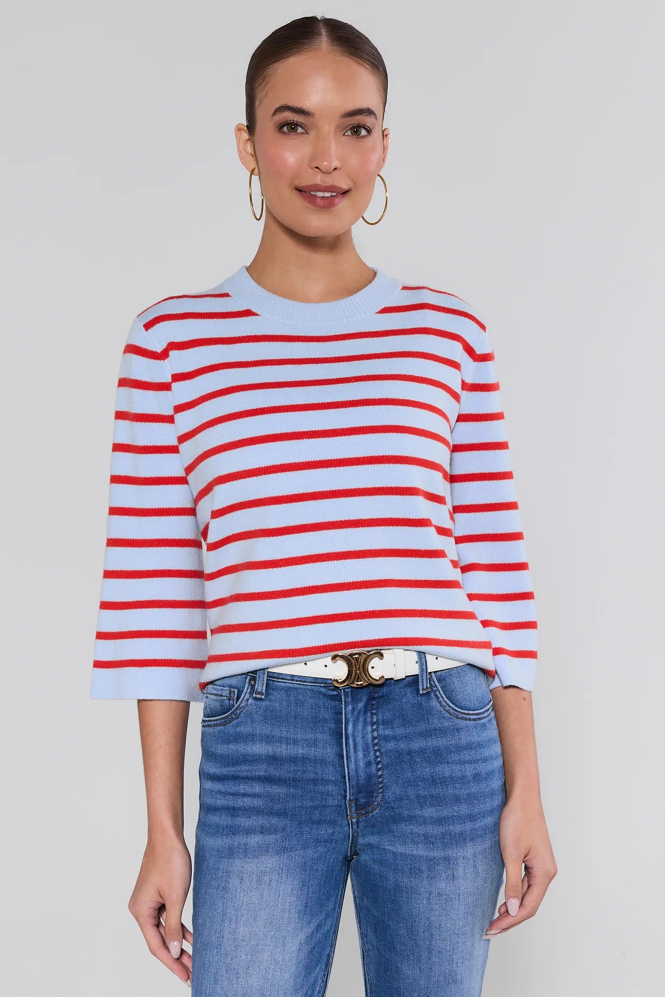 Woman wearing a red and white striped sweater with blue jeans on a plain background
