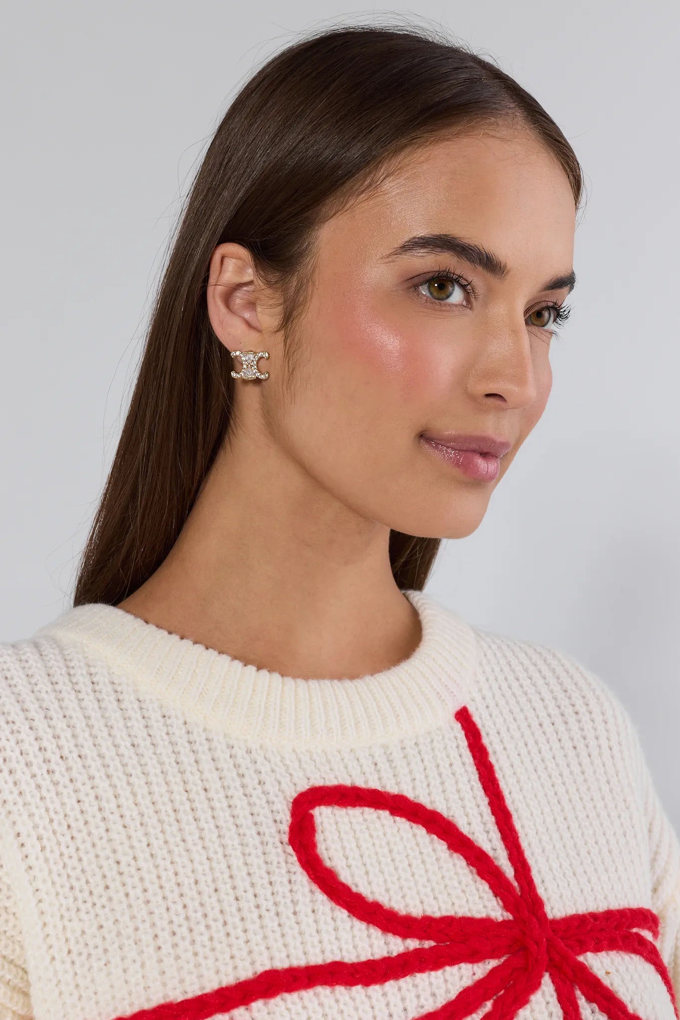Woman wearing a cream sweater with a red bow design on a plain background
