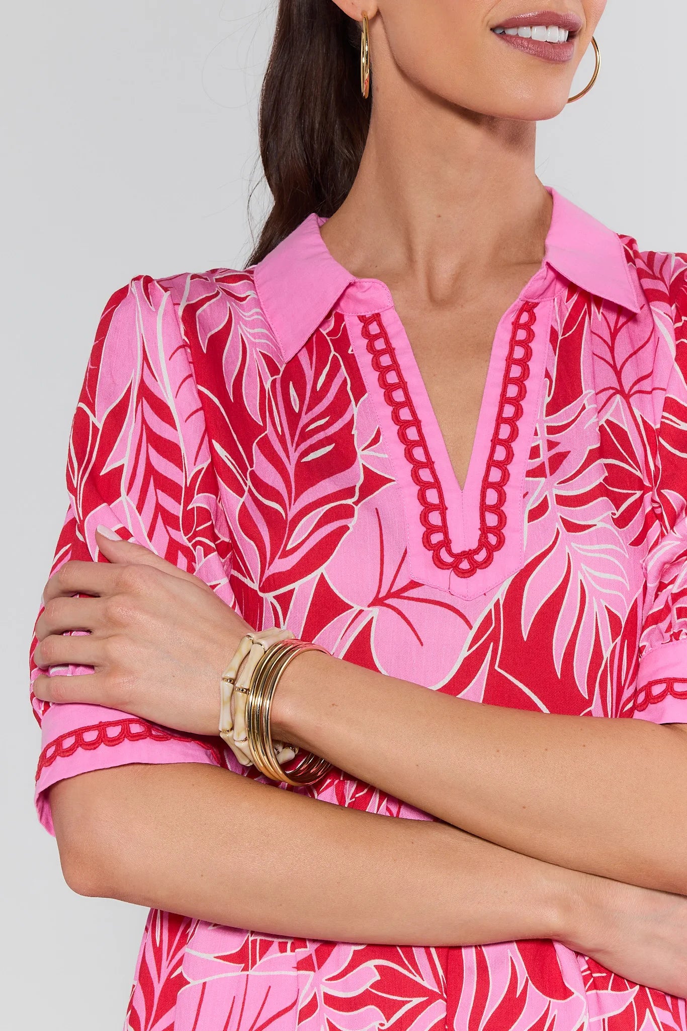 Woman wearing a pink and red patterned blouse with gold bracelets on a white background