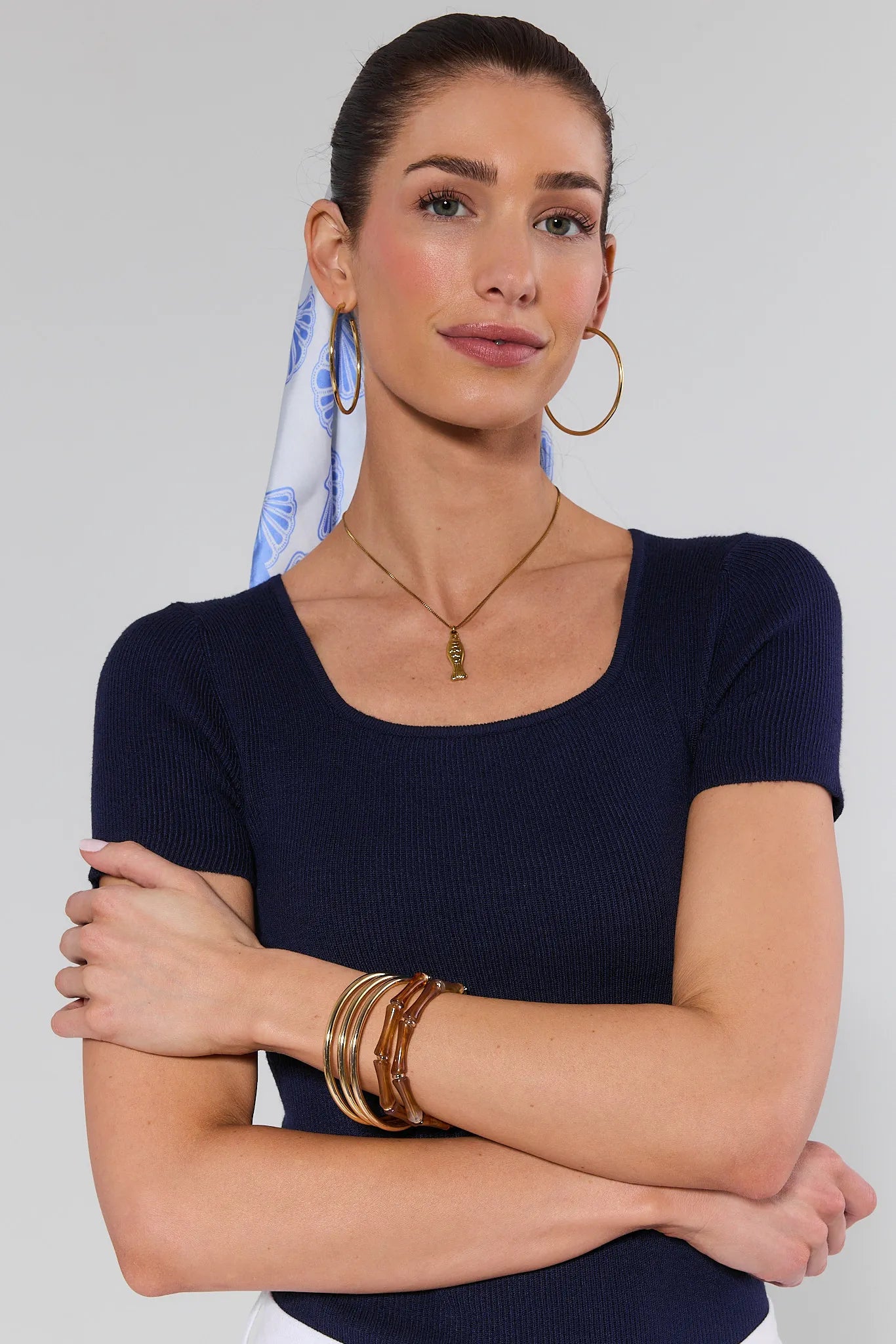 Woman wearing a navy blue top with gold jewelry against a plain background