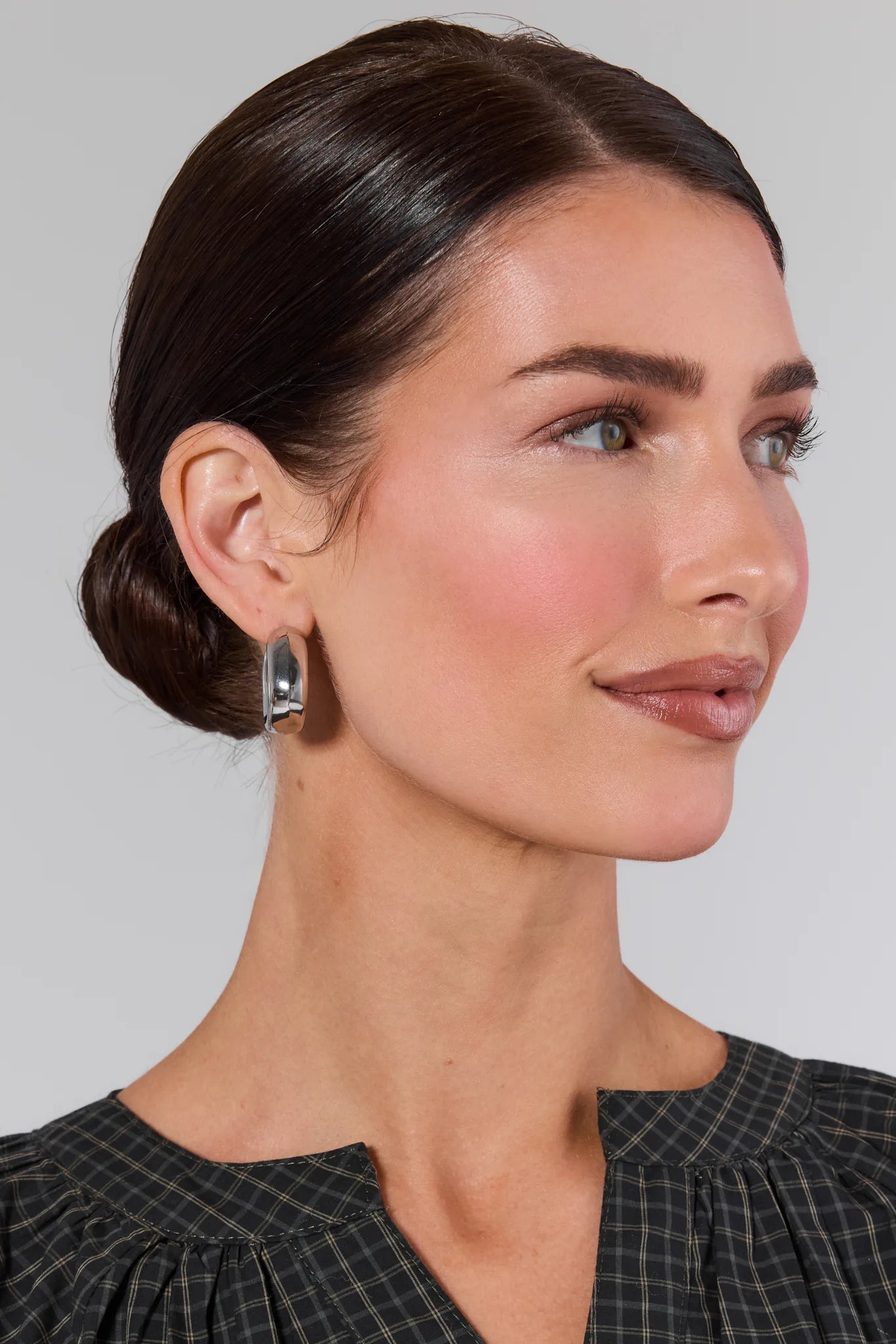 Woman with a side bun wearing earrings against a plain background Aurora Silver Hoop Earrings