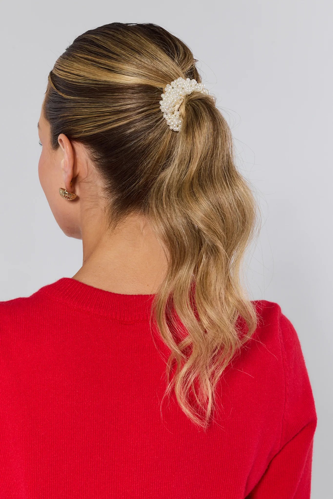 Person with a ponytail wearing a red sweater against a plain background