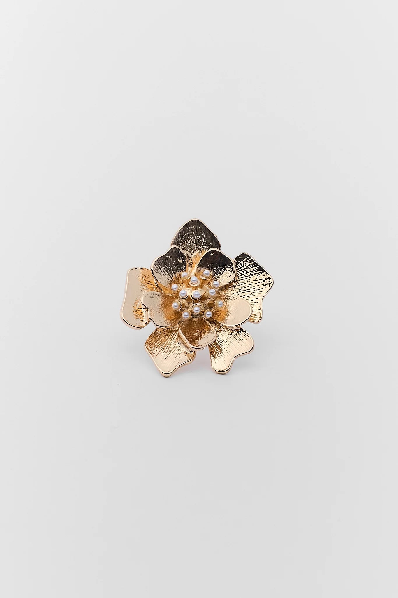 Gold flower-shaped brooch with pearl center on a light gray background