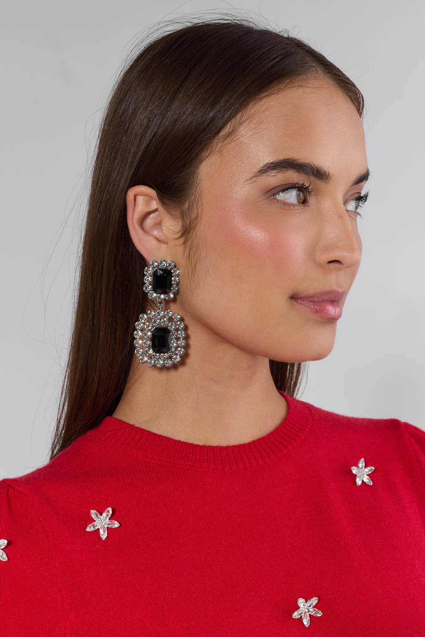 Woman wearing large black and silver earrings with a red sweater featuring white floral patterns.