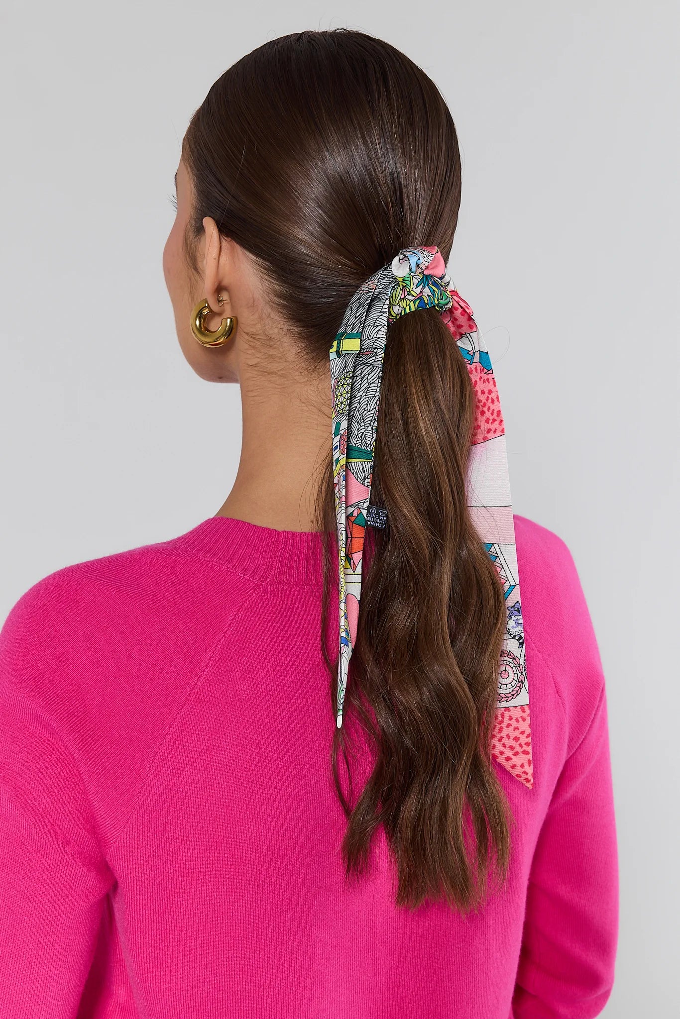 Person with a colorful scrunchie in their hair wearing a pink sweater on a plain background