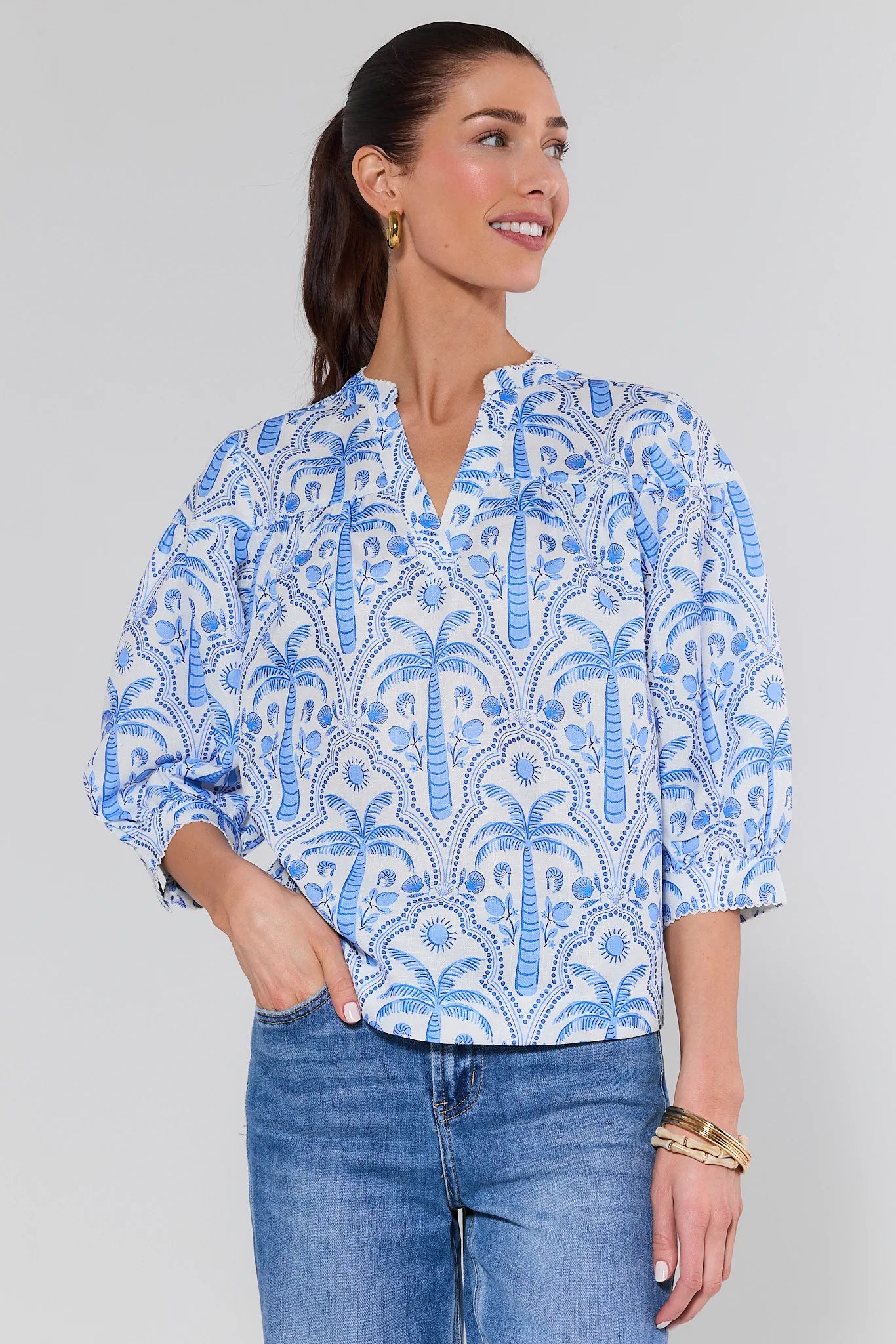Woman wearing a blue patterned blouse and jeans on a gray background