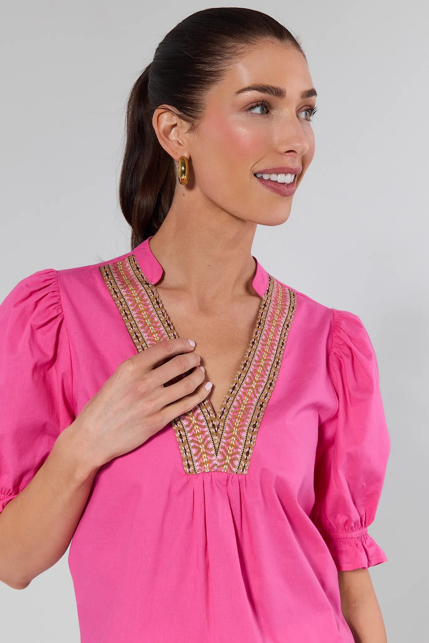 Woman wearing a pink blouse with intricate embroidery on a gray background