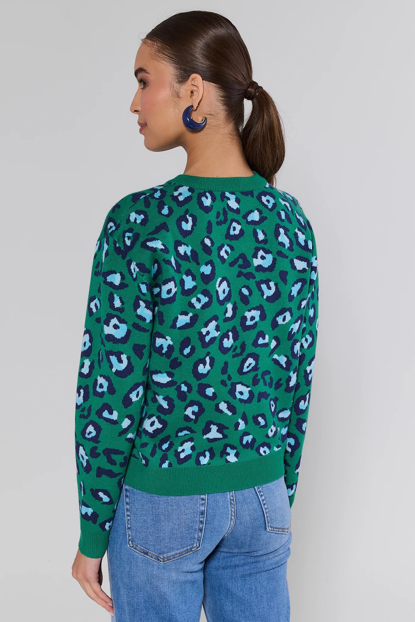 Person wearing a green leopard print sweater and blue jeans on a plain background