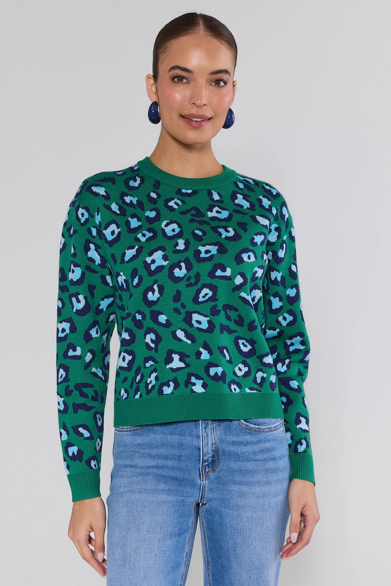 Woman wearing a green sweater with blue animal print pattern and blue jeans on a white background