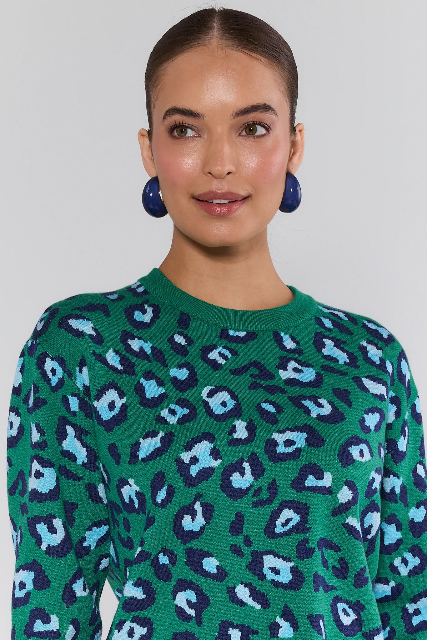 Woman wearing a green sweater with blue and purple leopard print pattern against a plain background