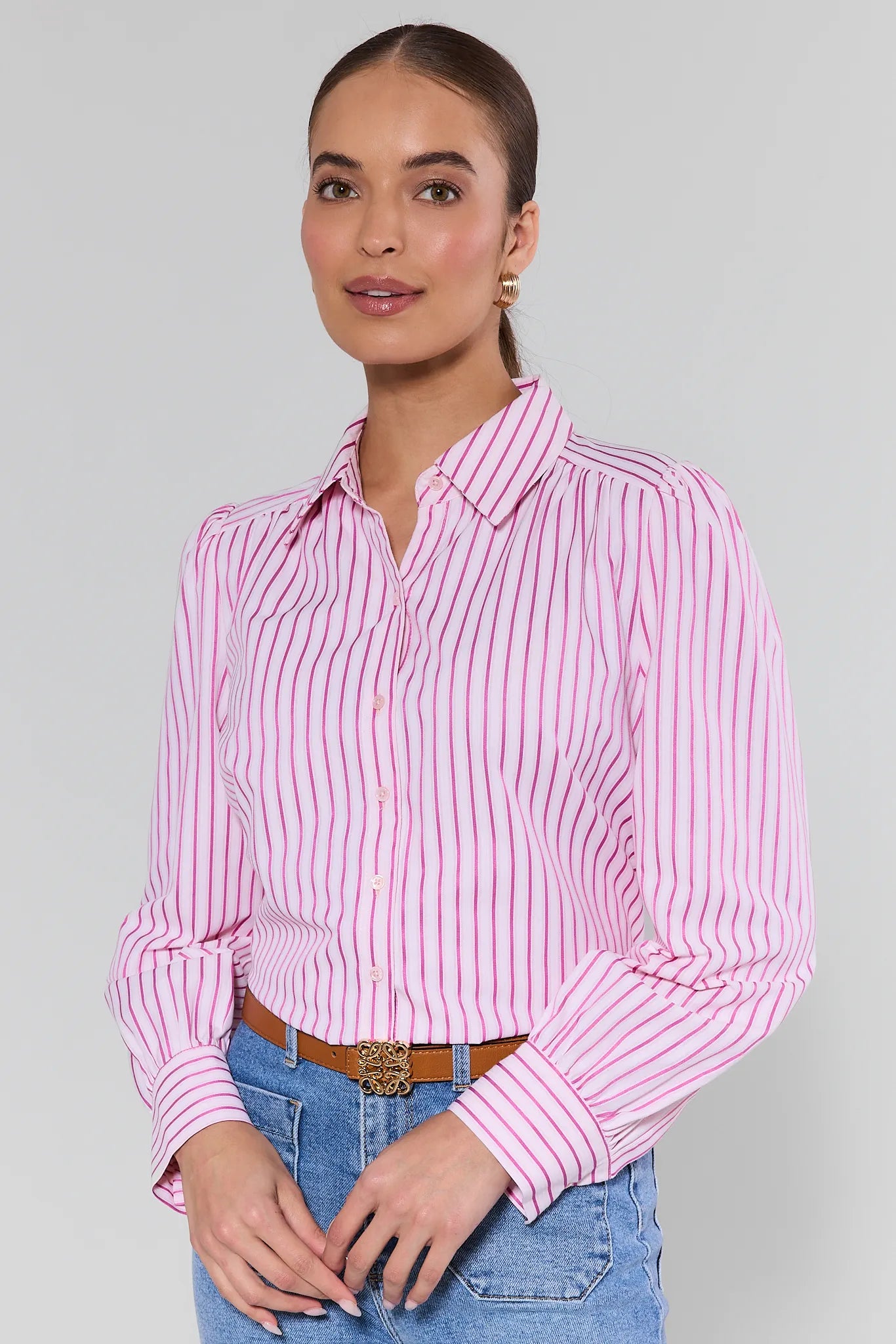Woman wearing a pink and white striped shirt with blue jeans on a gray background