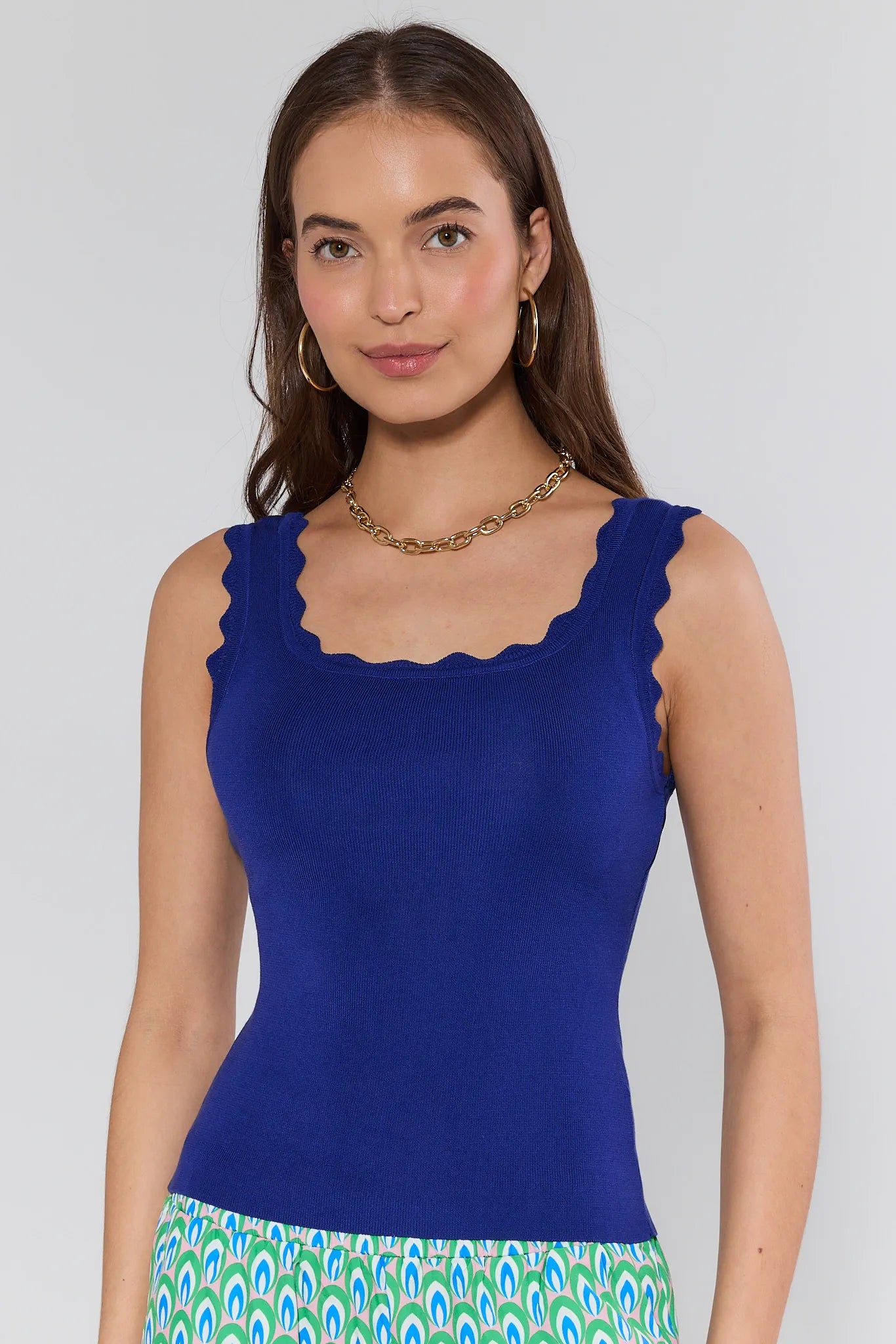 Woman wearing a blue sleeveless top with a scalloped neckline on a plain background