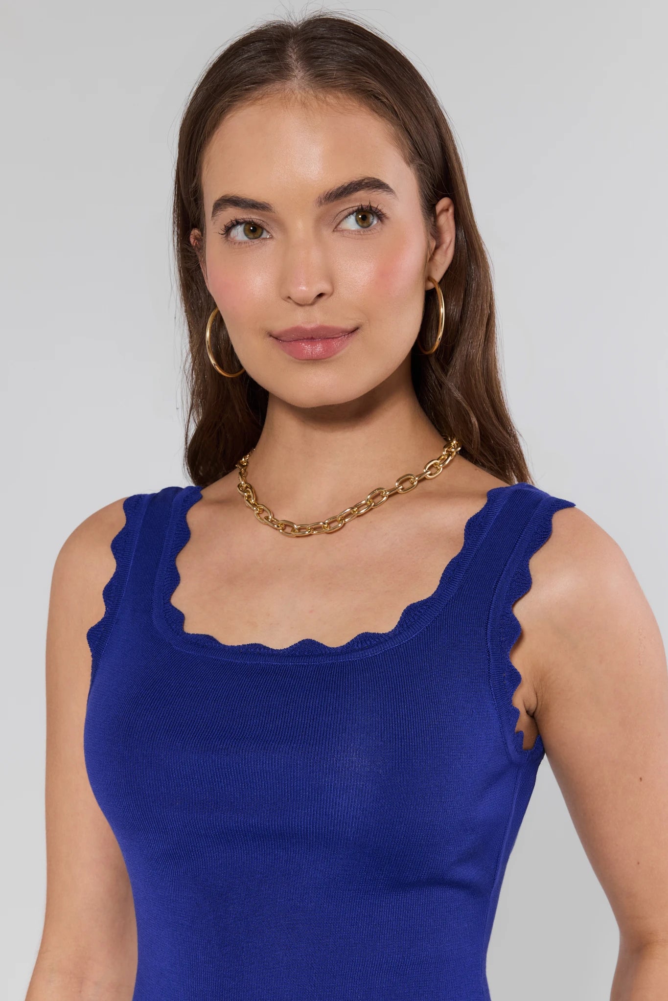 Woman wearing a top with scalloped edges and a gold necklace on a gray background