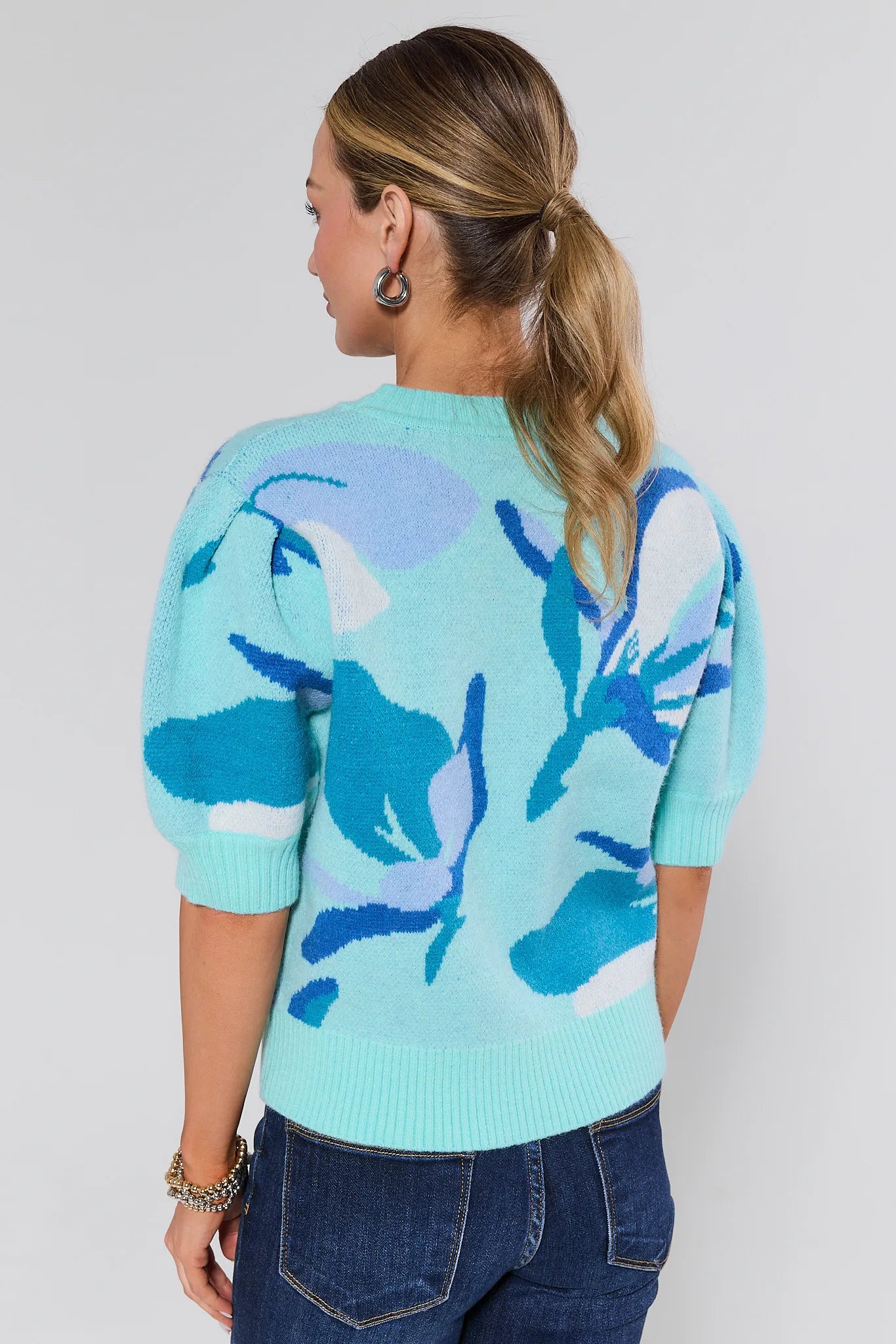 Woman wearing a light blue sweater with floral patterns on a plain background