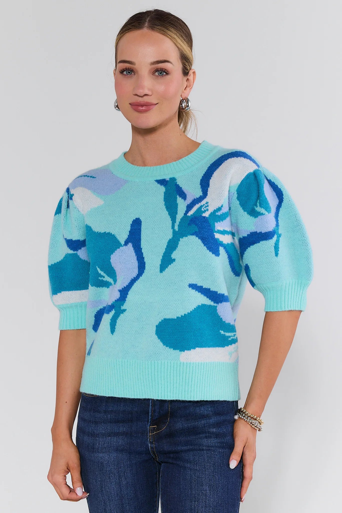Woman wearing a light blue sweater with abstract blue and white designs on a plain background