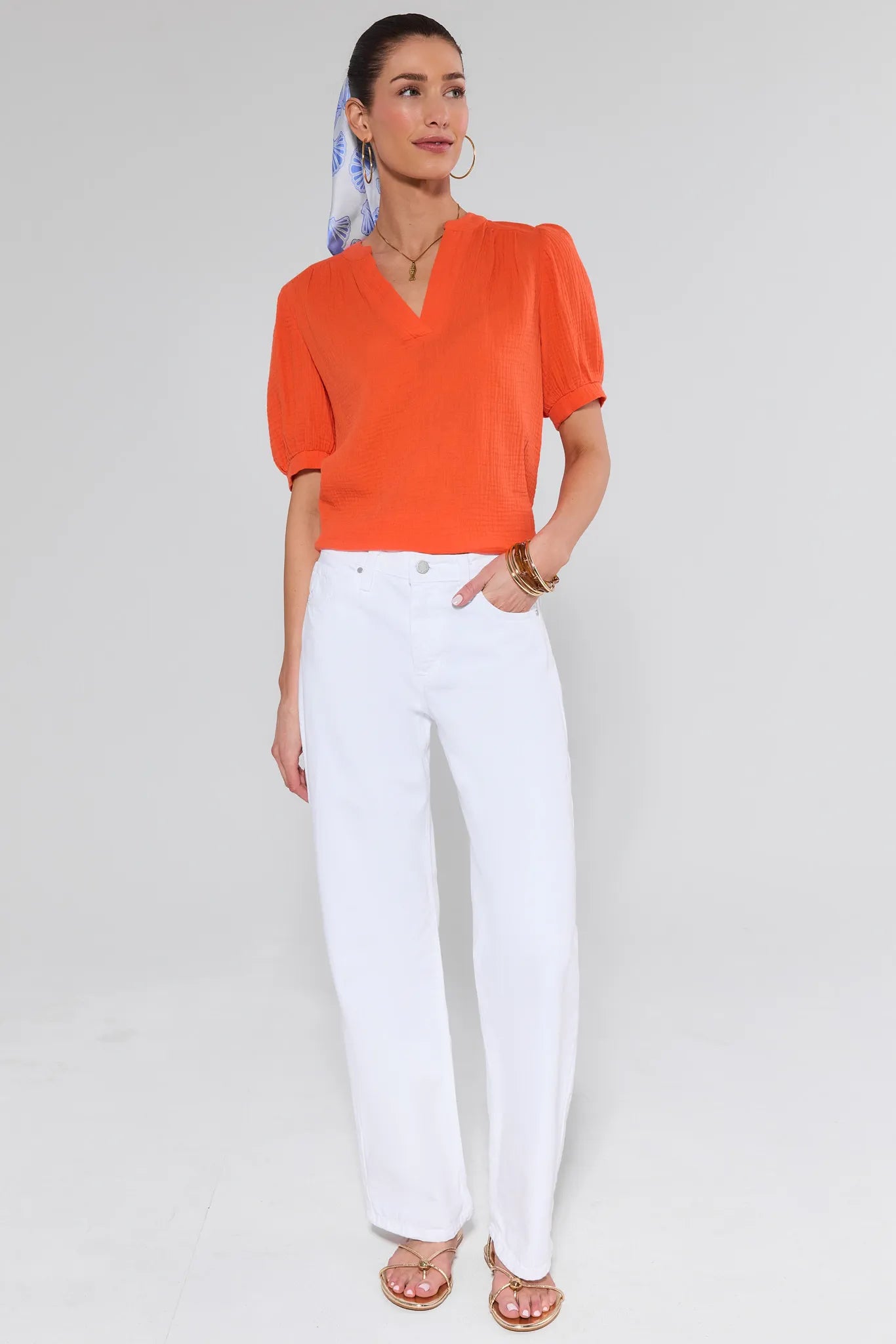 Woman wearing an orange top and white pants on a plain background