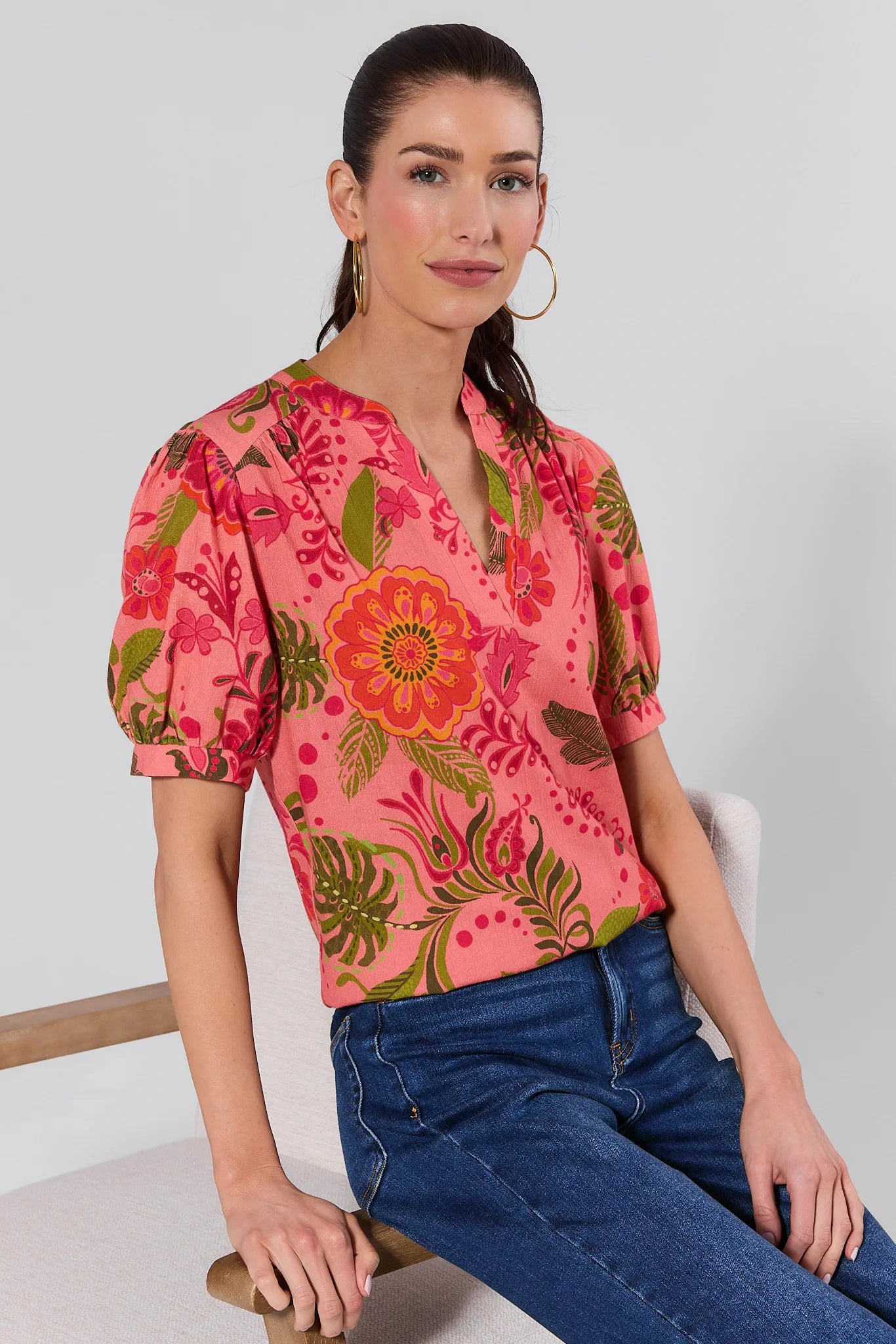 Woman wearing a pink floral blouse sitting on a chair.