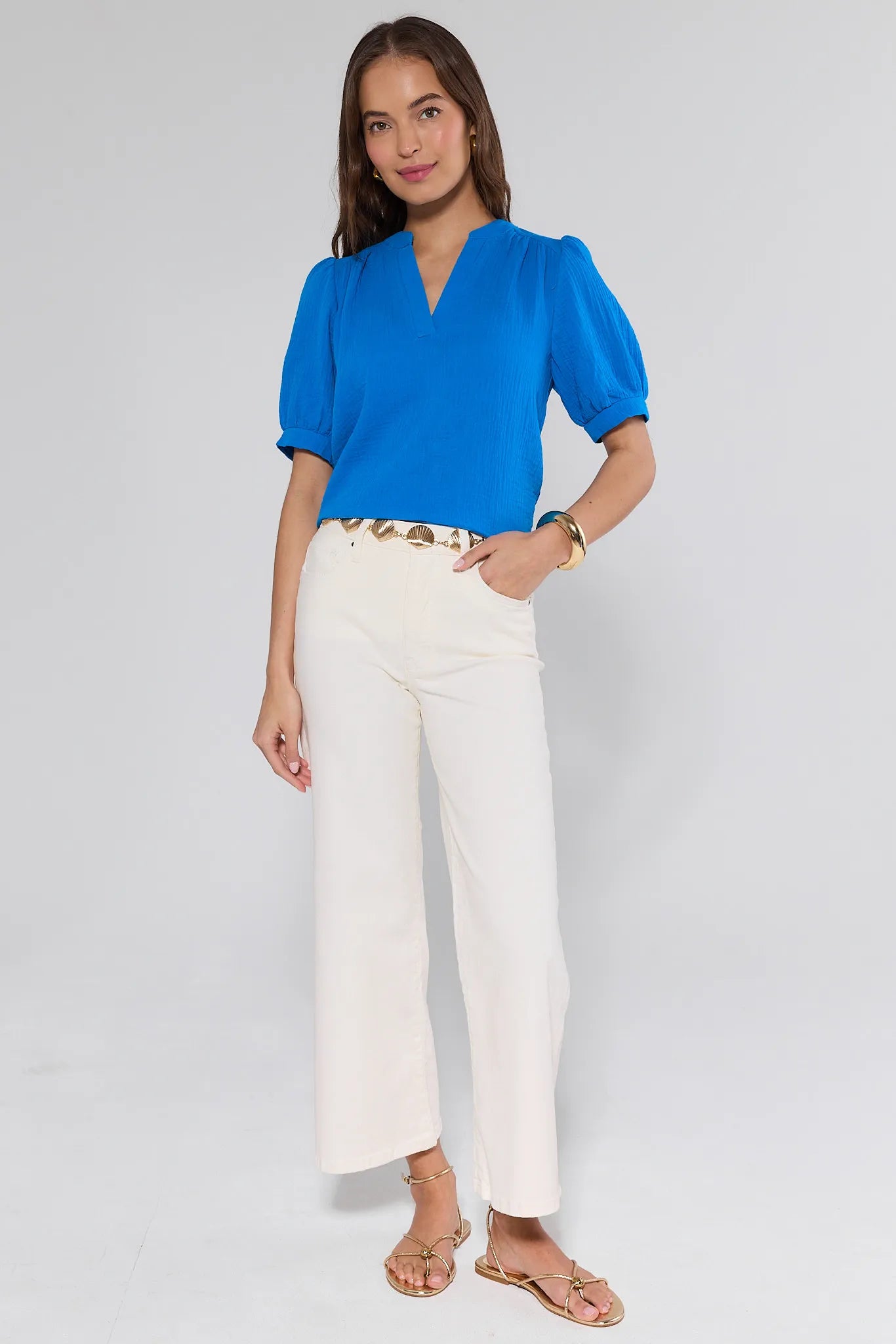 Woman wearing a blue blouse and white pants on a gray background