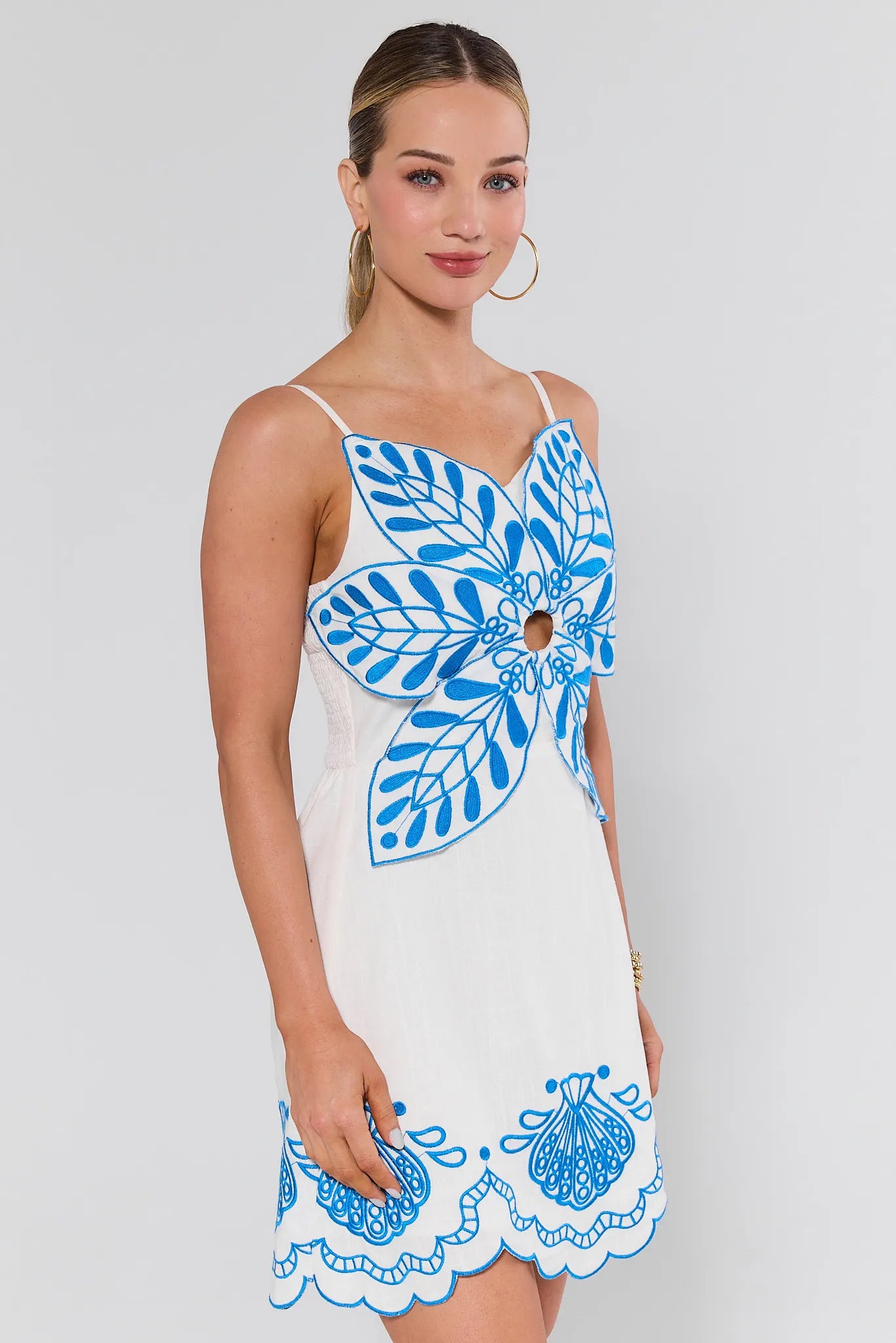 Woman wearing a white dress with blue floral patterns on a plain background