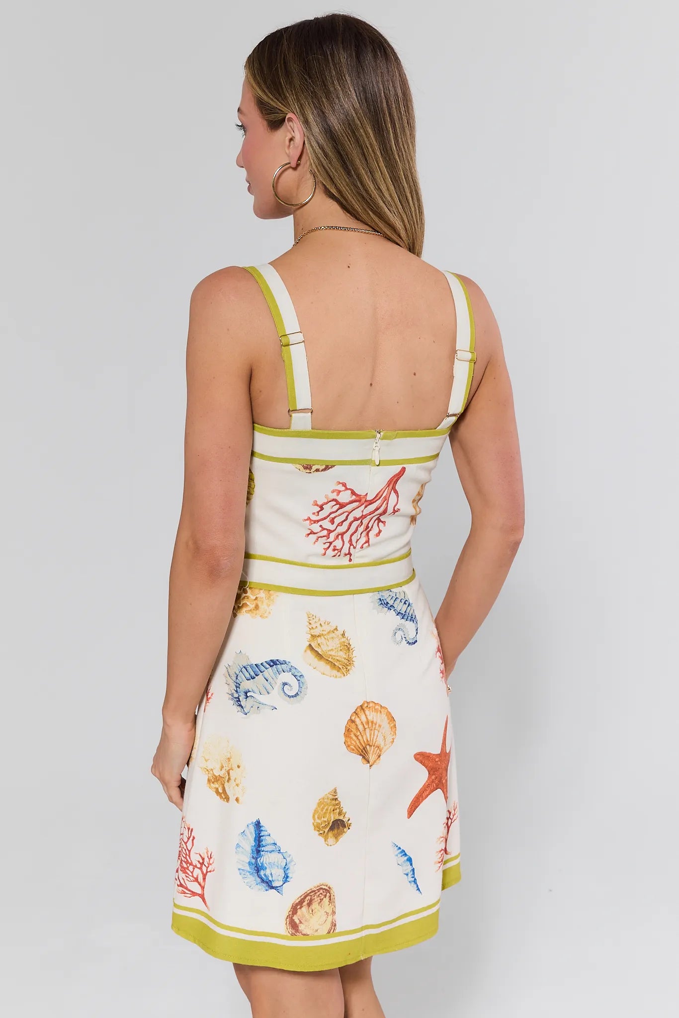 Woman wearing a sleeveless dress with a colorful shell pattern on a plain background