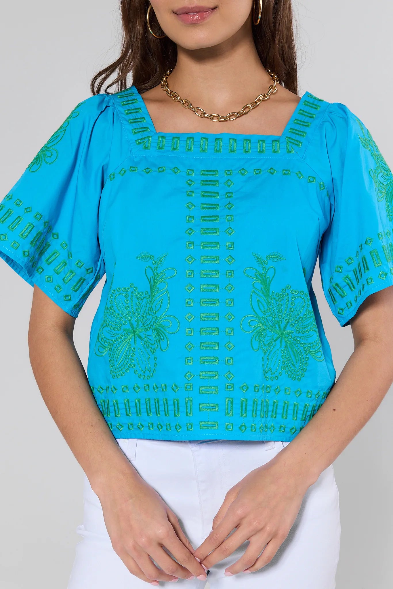 Blue top with green patterns worn by a person on a plain background