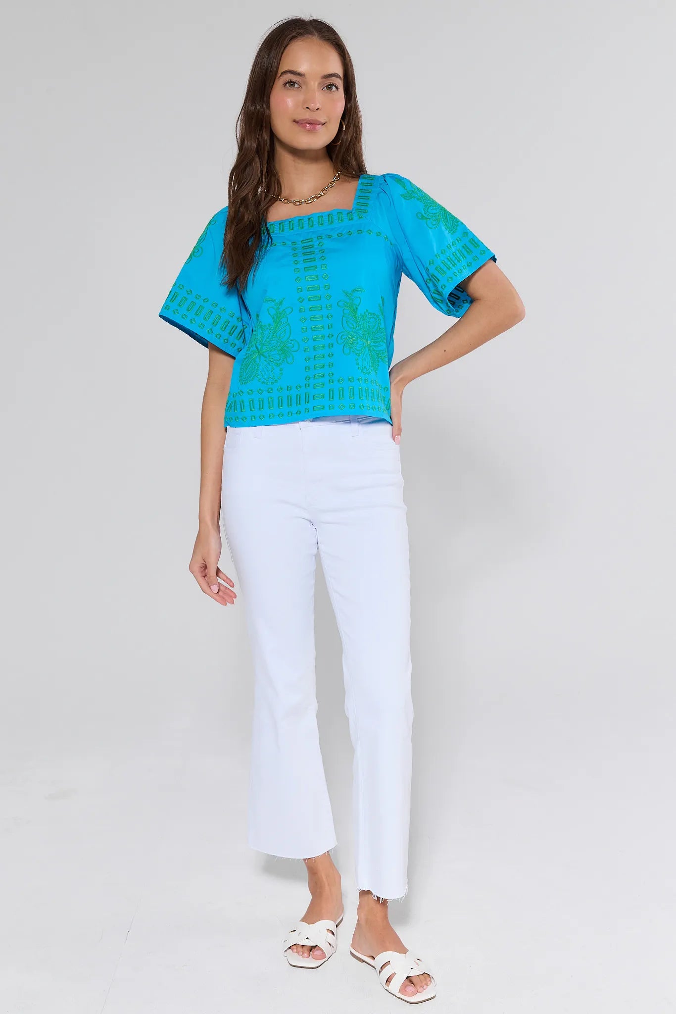 Woman wearing a blue top and white pants on a gray background