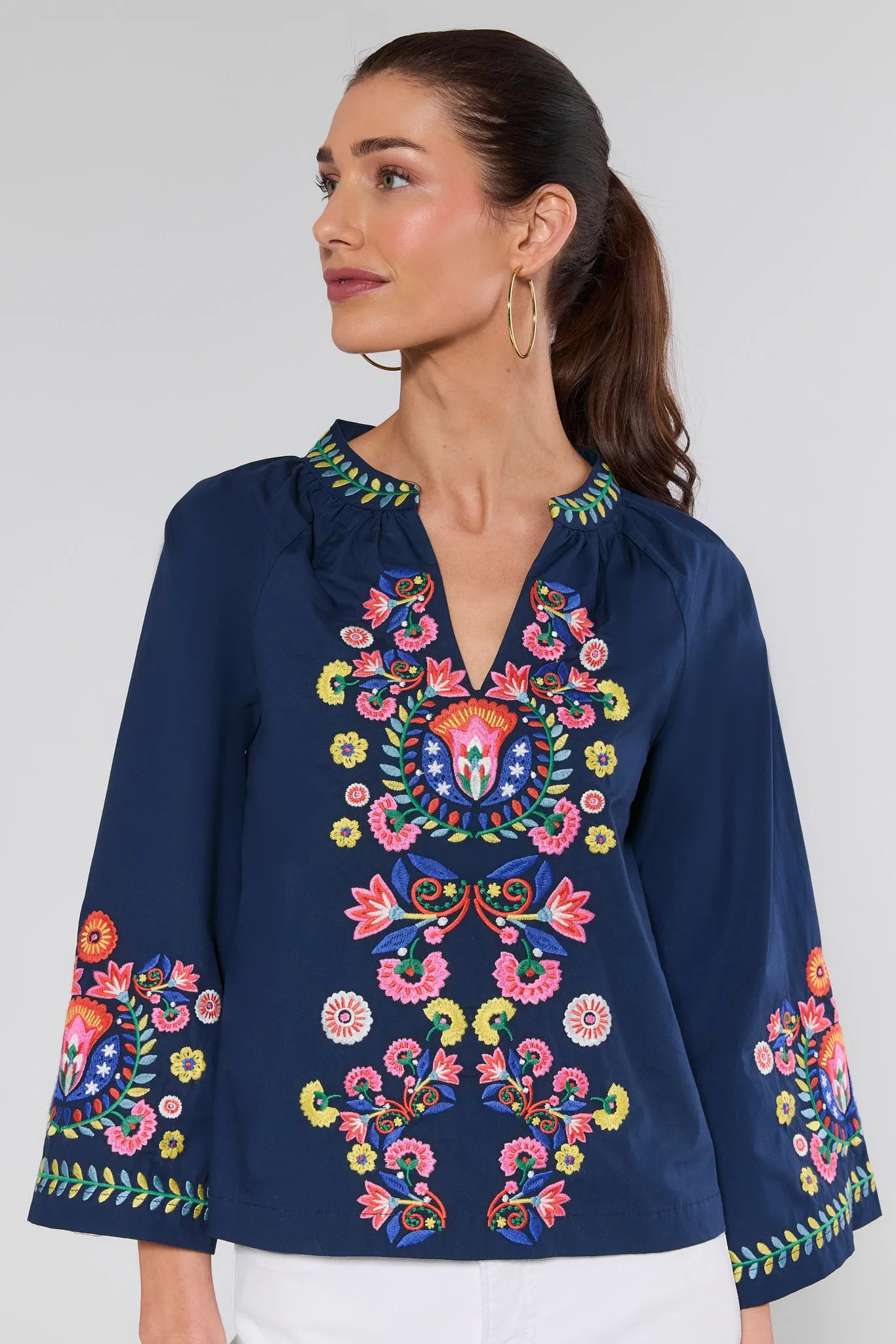 Woman wearing a navy blue blouse with colorful floral embroidery on a plain background