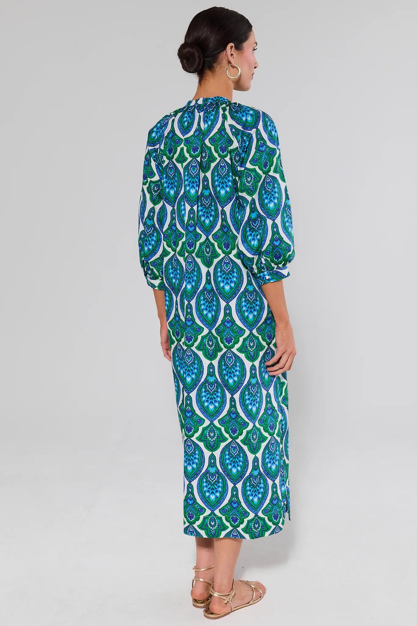 Woman standing wearing a green and blue patterned dress on a white background