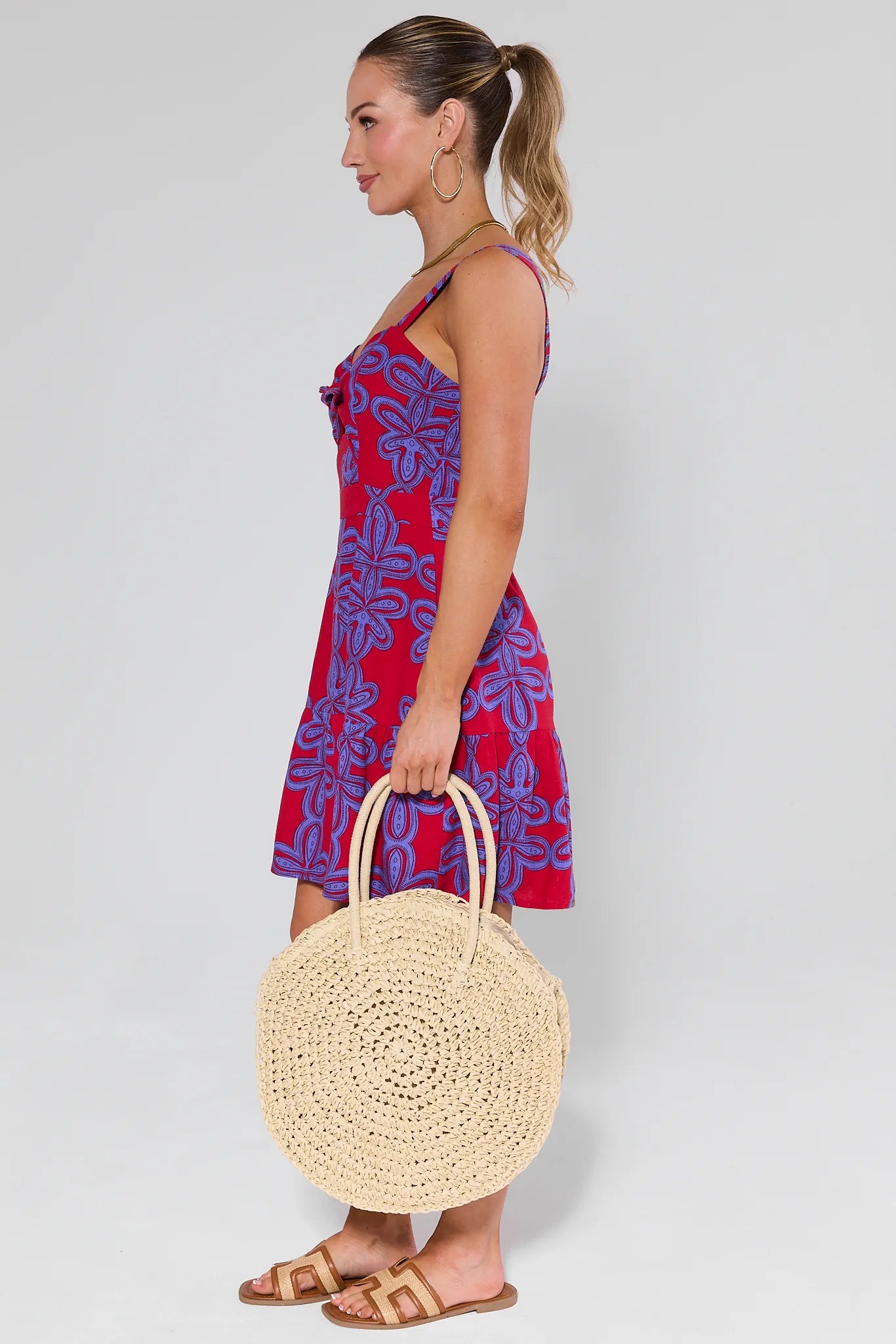 Woman in a red and blue dress holding a Josie Raffia Woven Bucket Bag against a white background