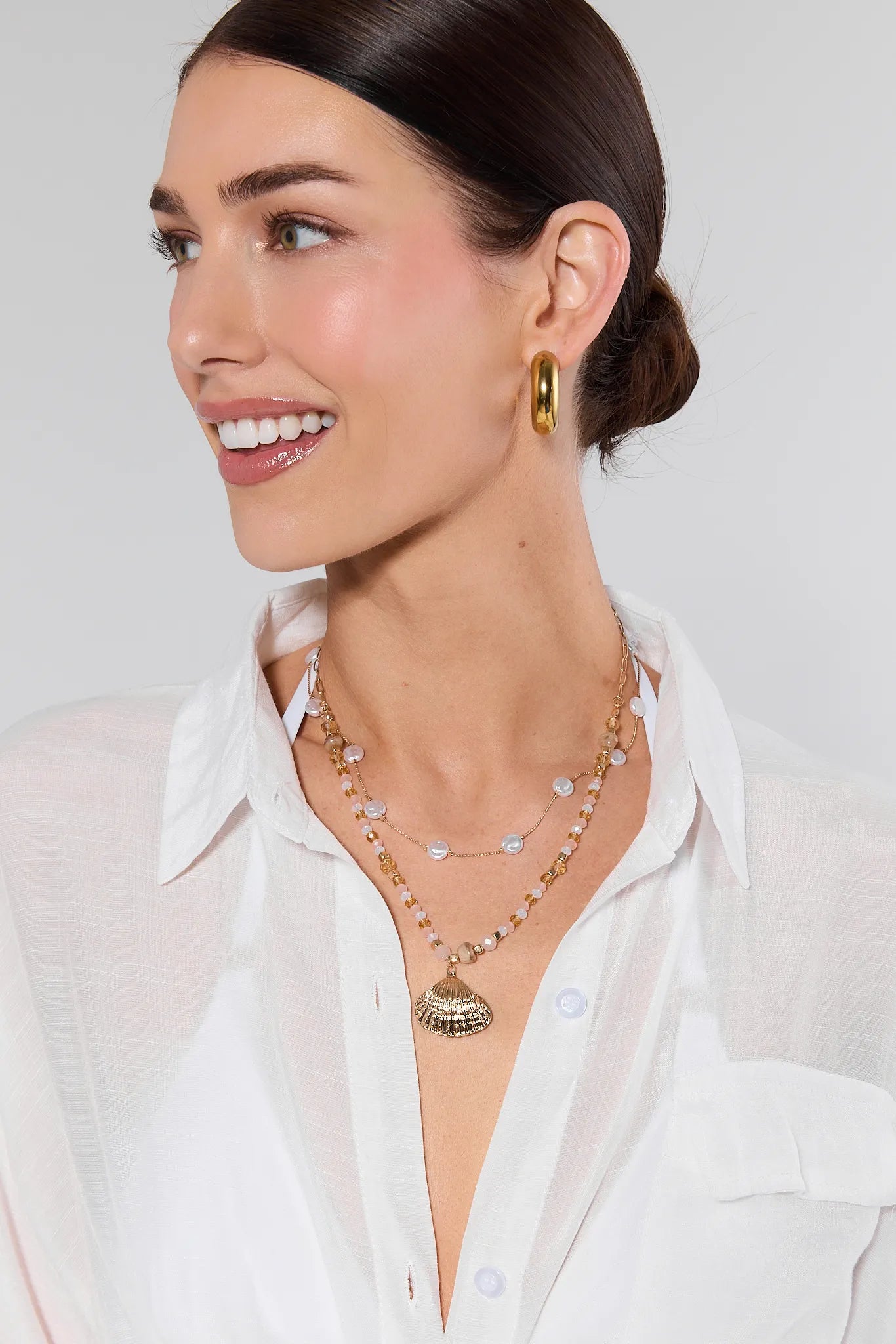 Woman wearing a white shirt and gold jewelry against a plain background
