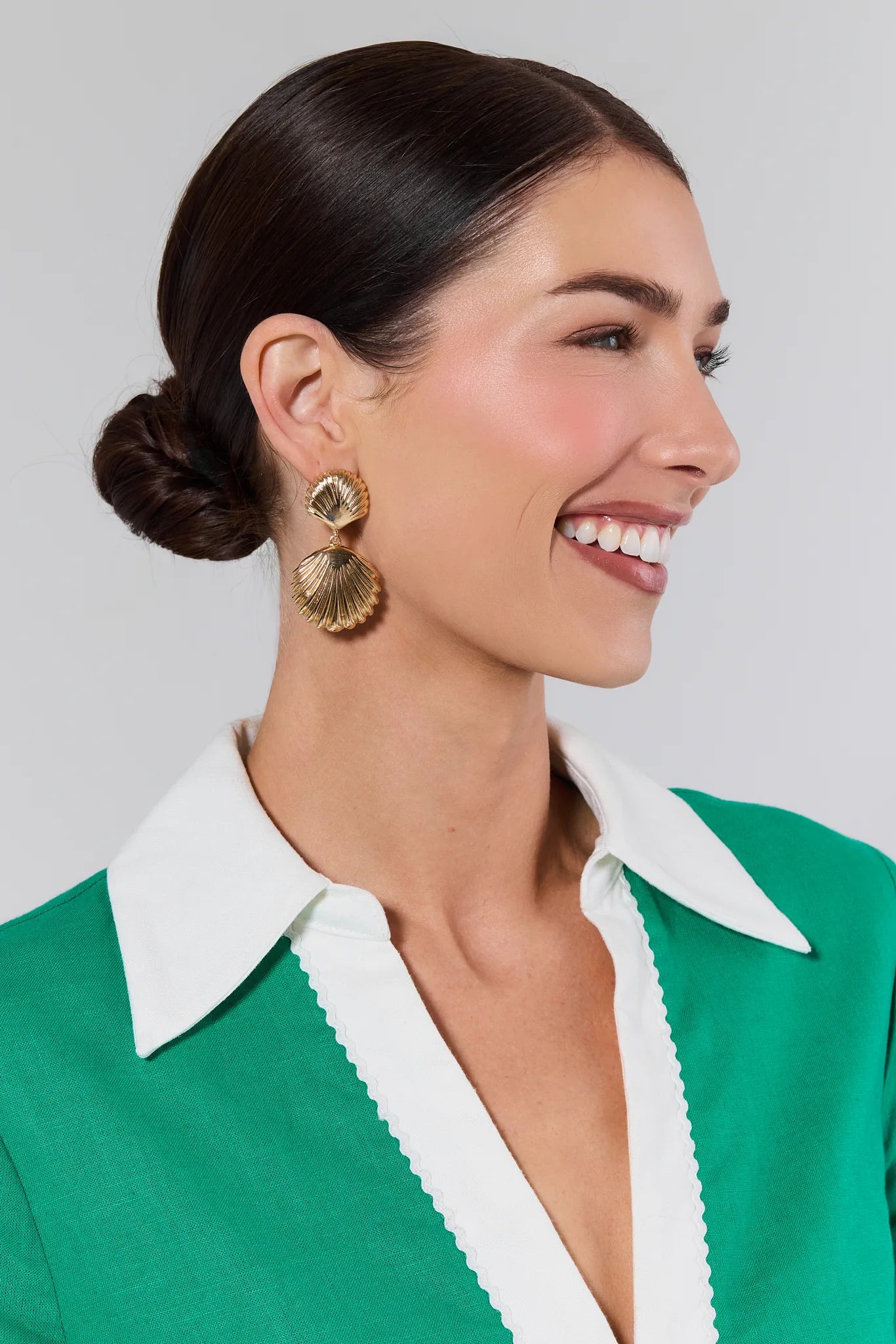 Woman wearing gold earrings with a green and white outfit on a plain background