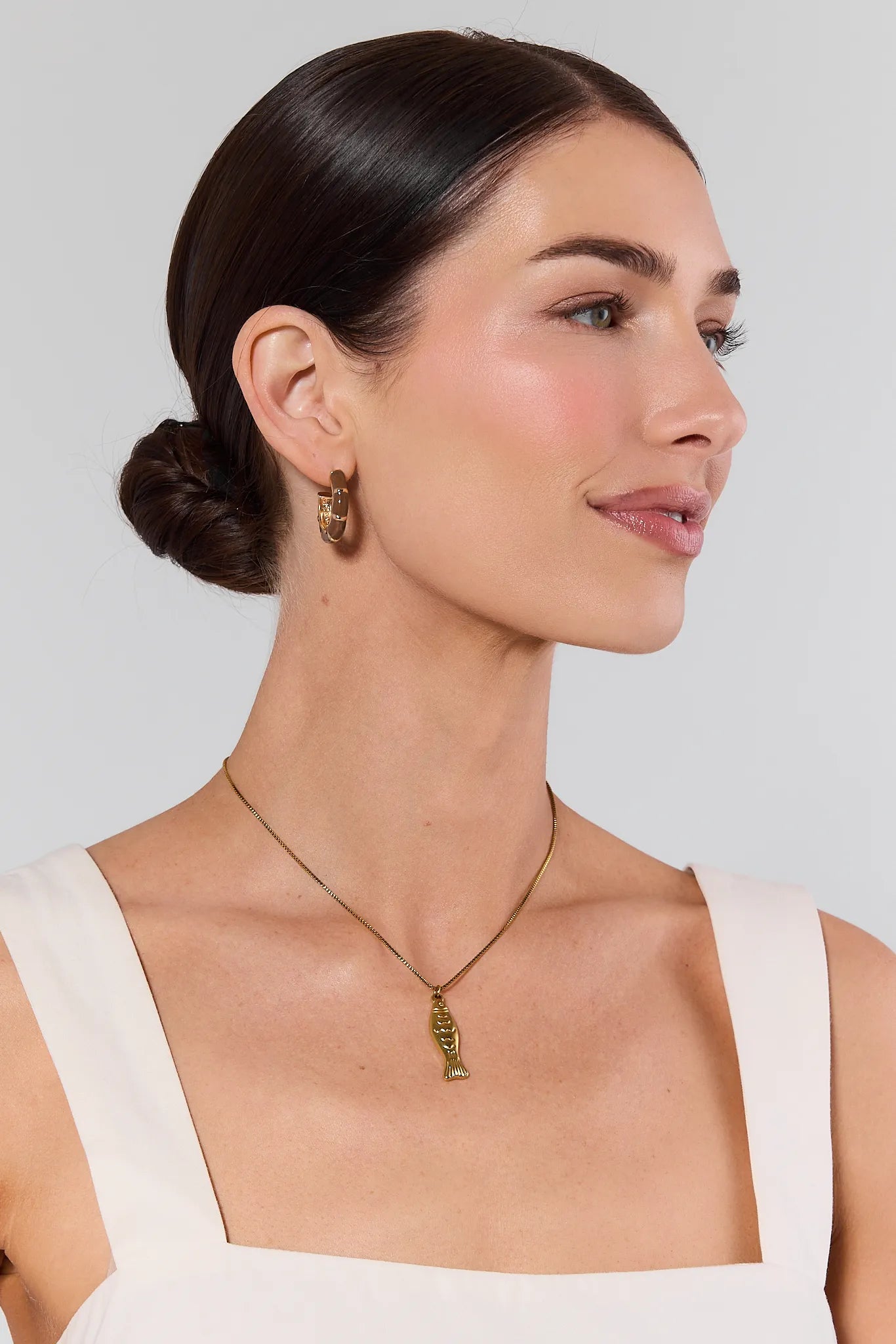 Woman wearing gold earrings and a necklace against a plain background