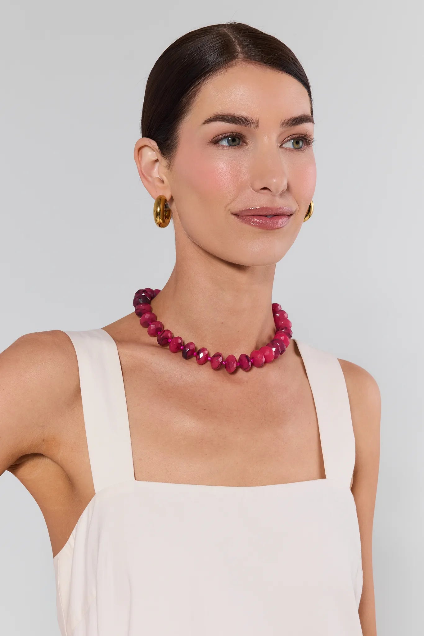 Woman wearing a pink beaded necklace against a plain background