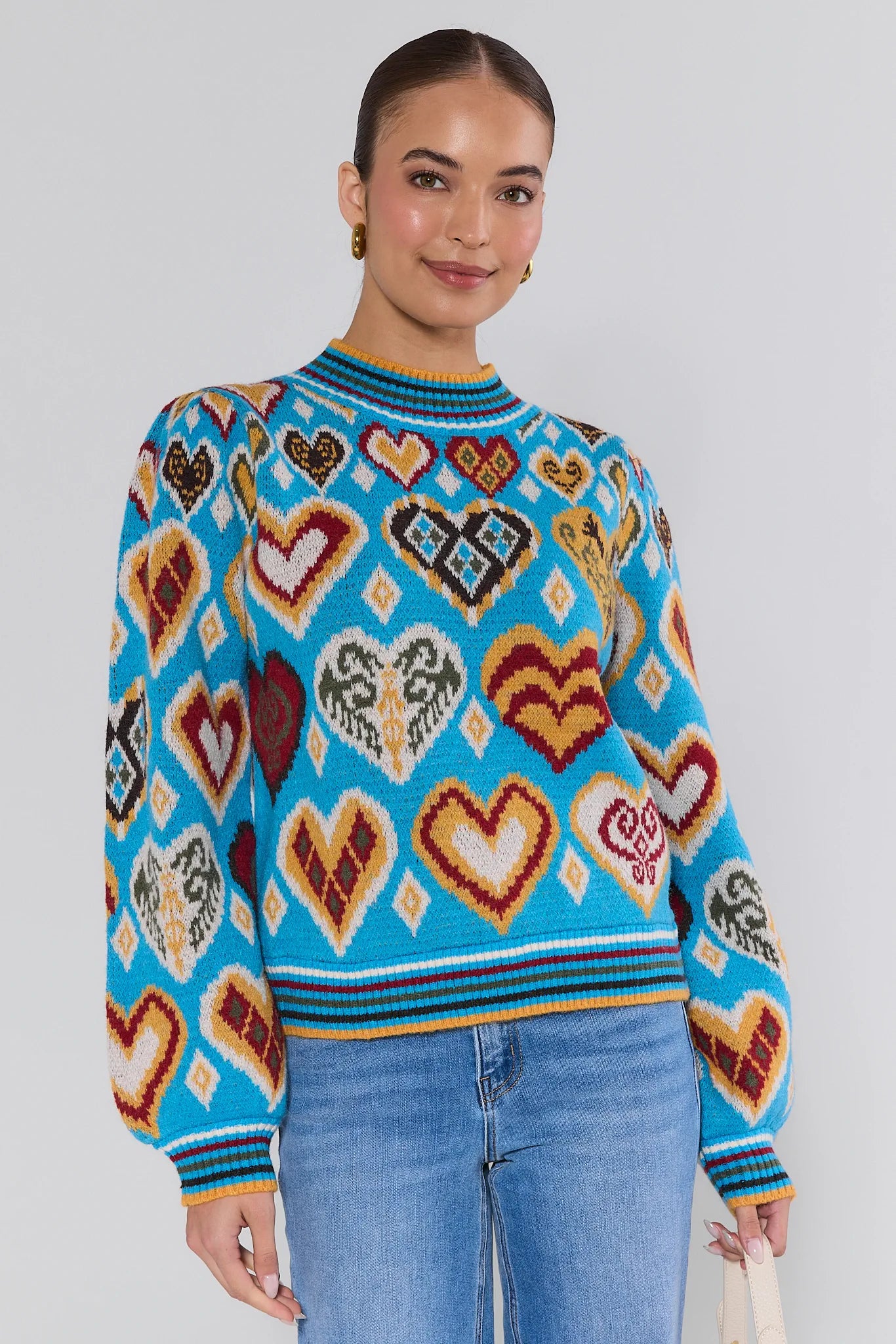 Woman wearing a colorful heart-patterned Cammie Blue Heart Knit Sweater against a plain background