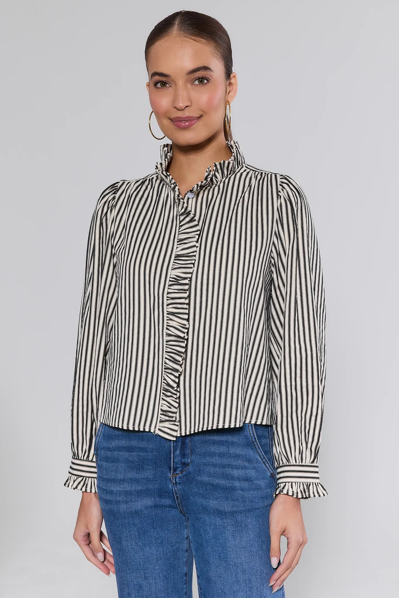 Woman wearing a Jacie Striped Ruffle Long Sleeve Top with blue jeans on a gray background