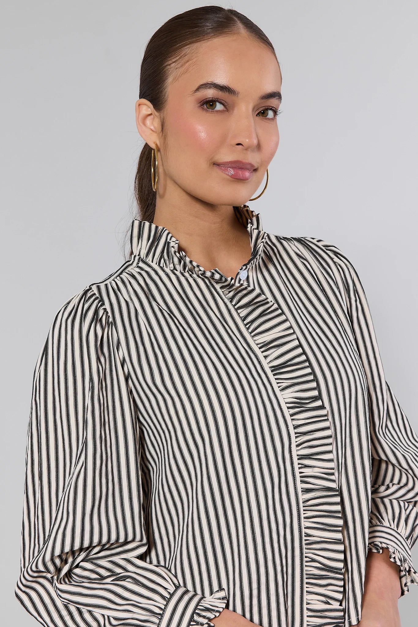 Woman wearing a Jacie Striped Ruffle Long Sleeve Top on a gray background