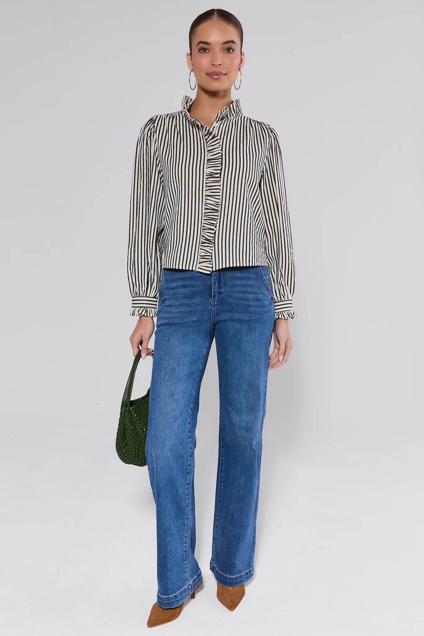Woman wearing a Jacie Striped Ruffle Long Sleeve Top with blue jeans and green bag on a gray background