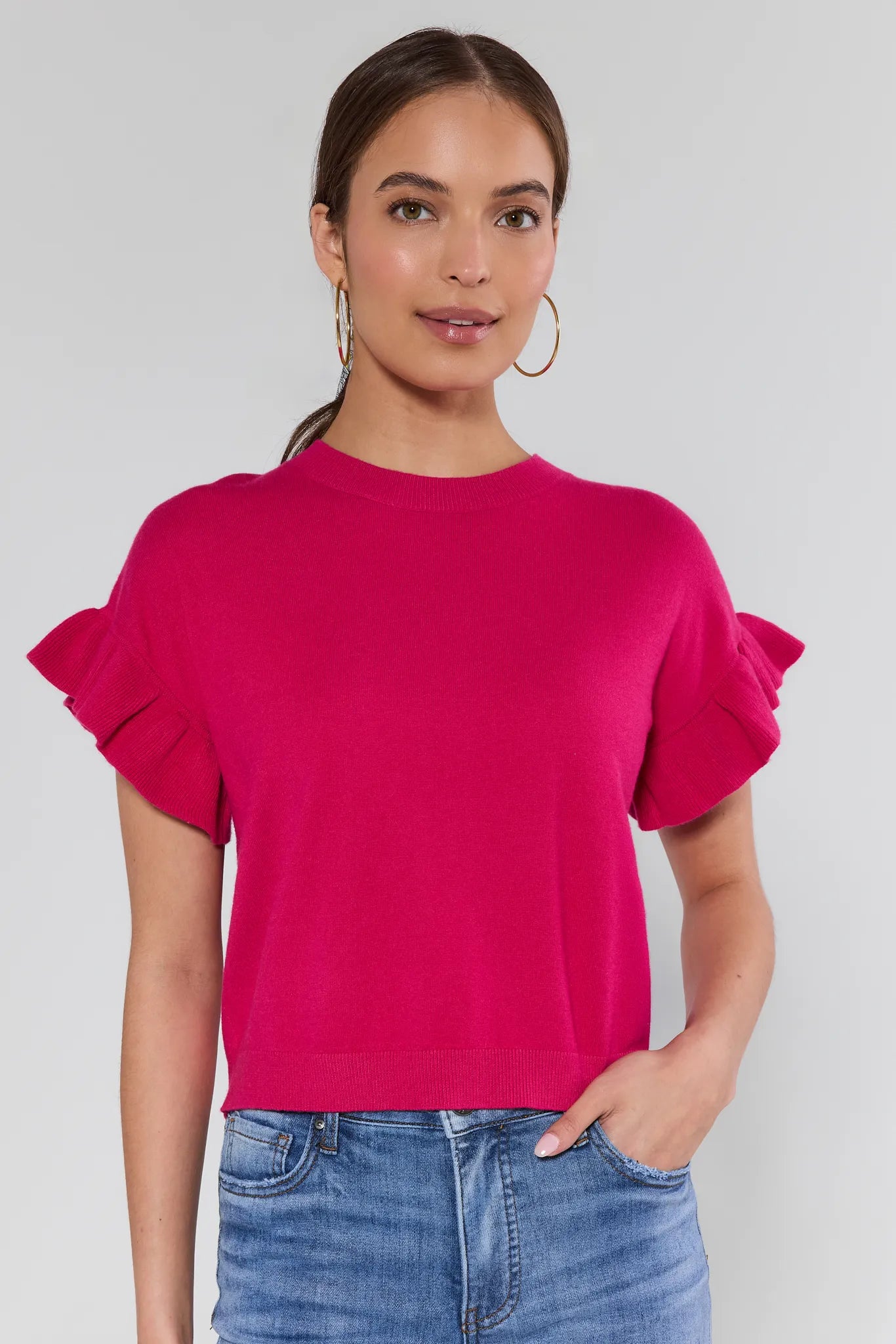 Woman wearing a bright pink top with ruffled sleeves against a plain background