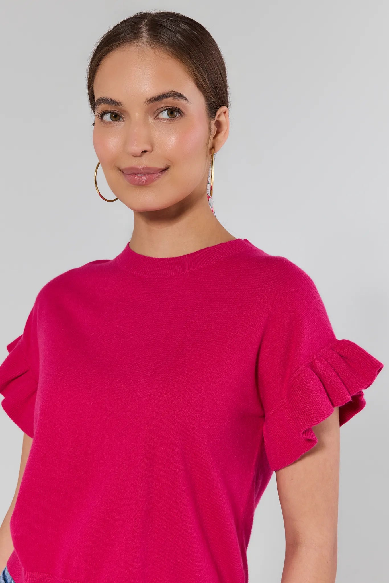 Woman wearing a bright pink top with ruffled sleeves against a plain background
