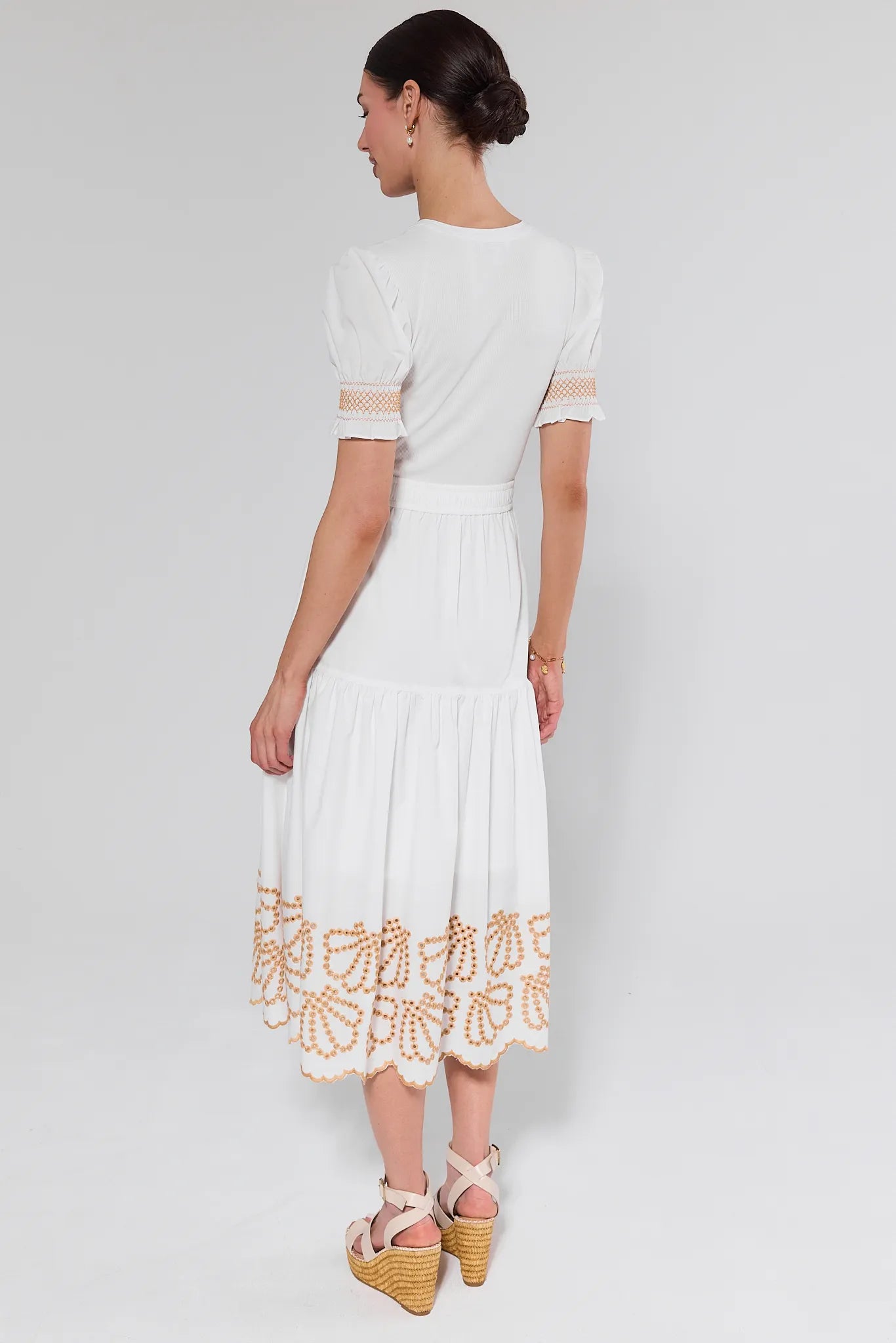 Woman wearing a white dress with gold accents on a plain background