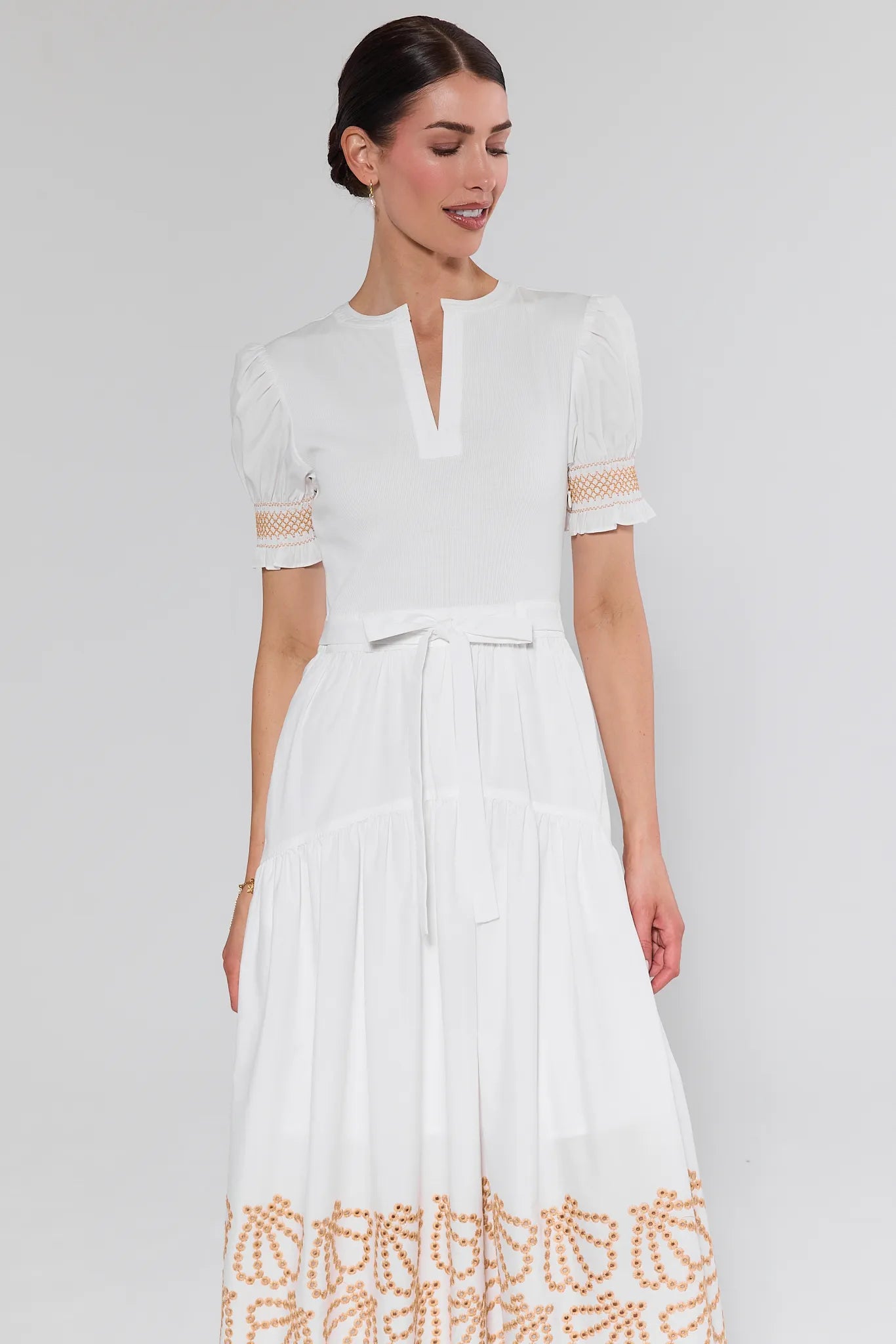 Woman wearing a white dress with gold embroidery on a plain background