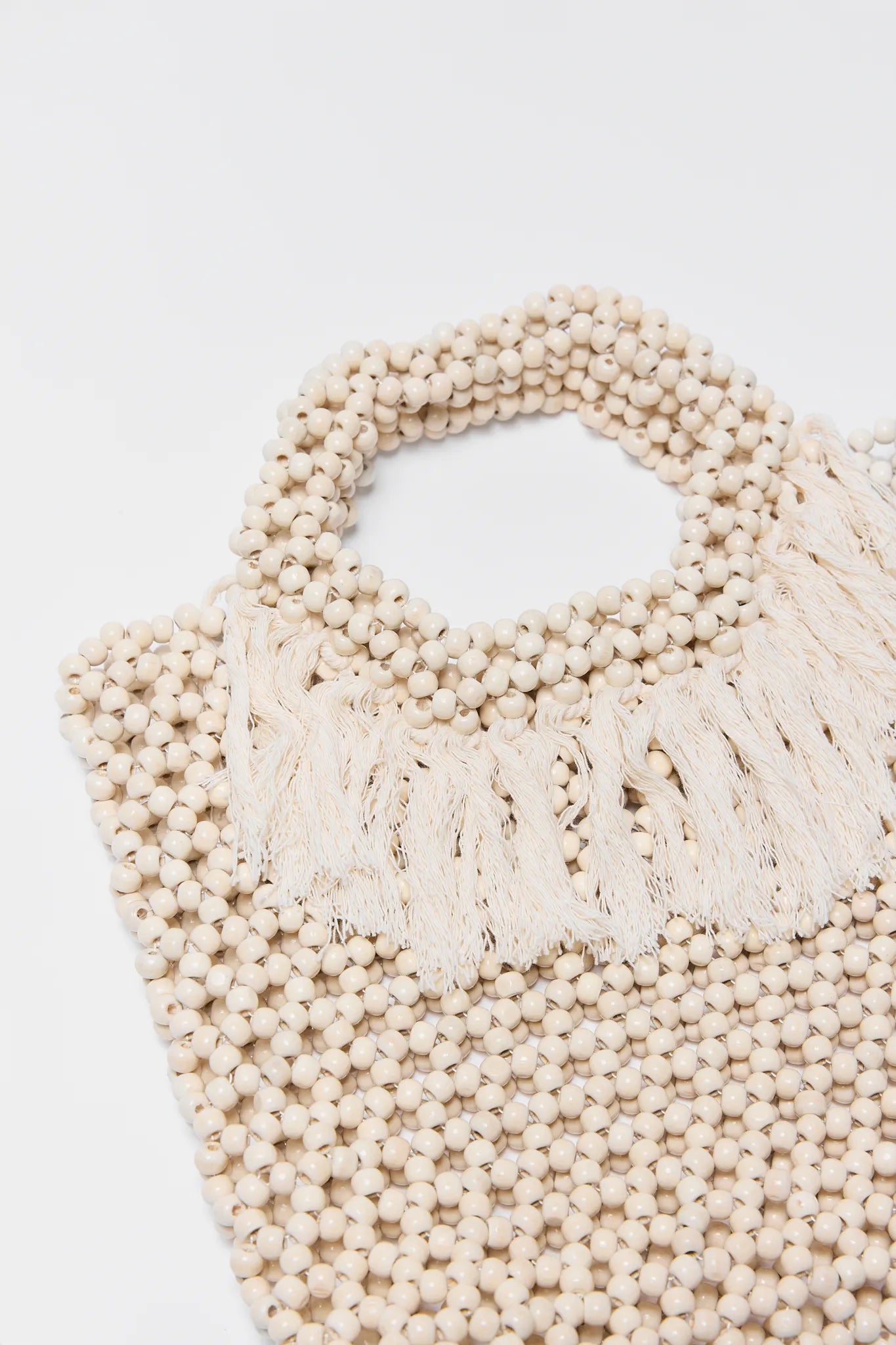 Beige woven Charlotte Beaded Fringe Bag with bead handle on a light gray background