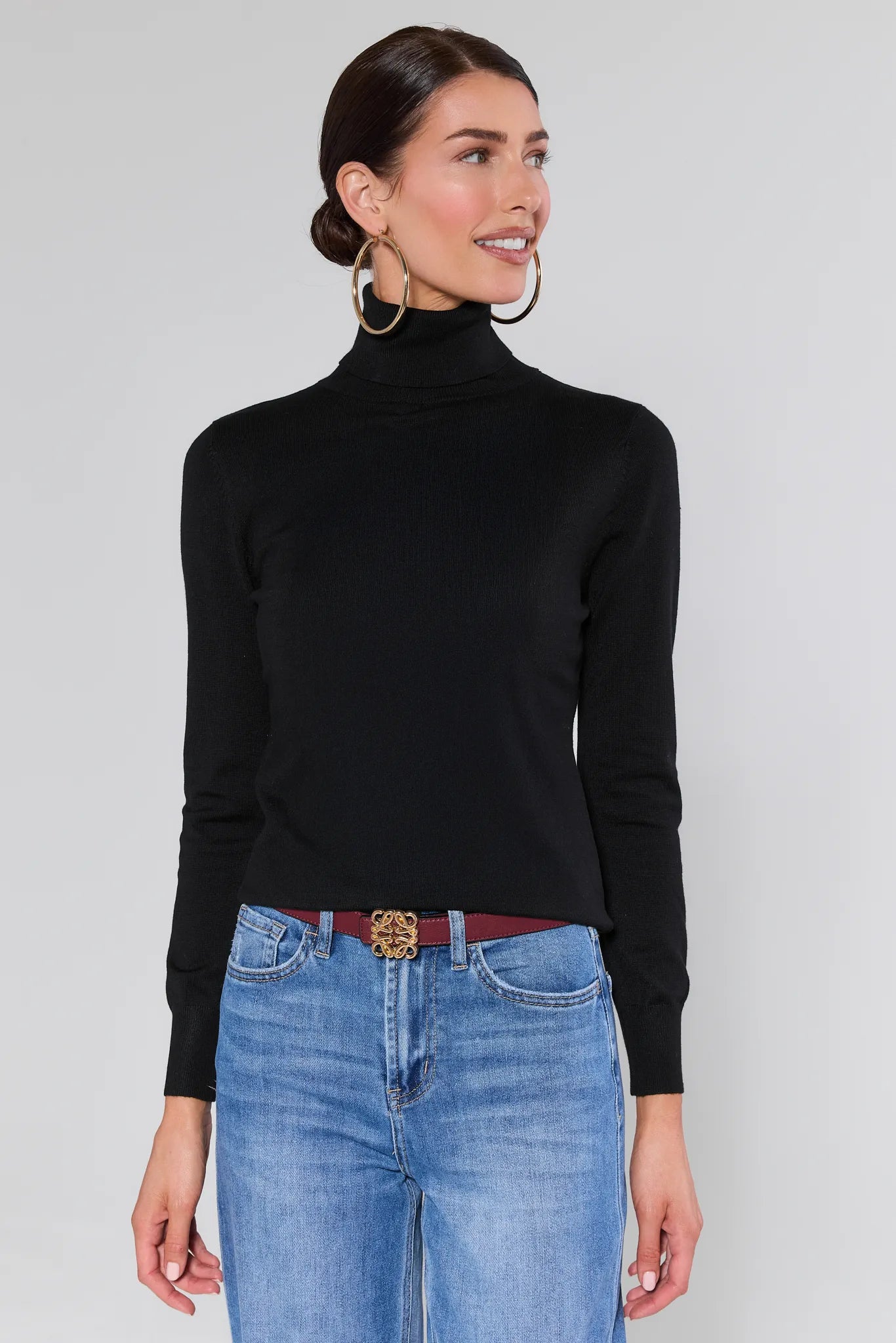 Woman wearing a Andrea Black Turtleneck Top and blue jeans against a plain background