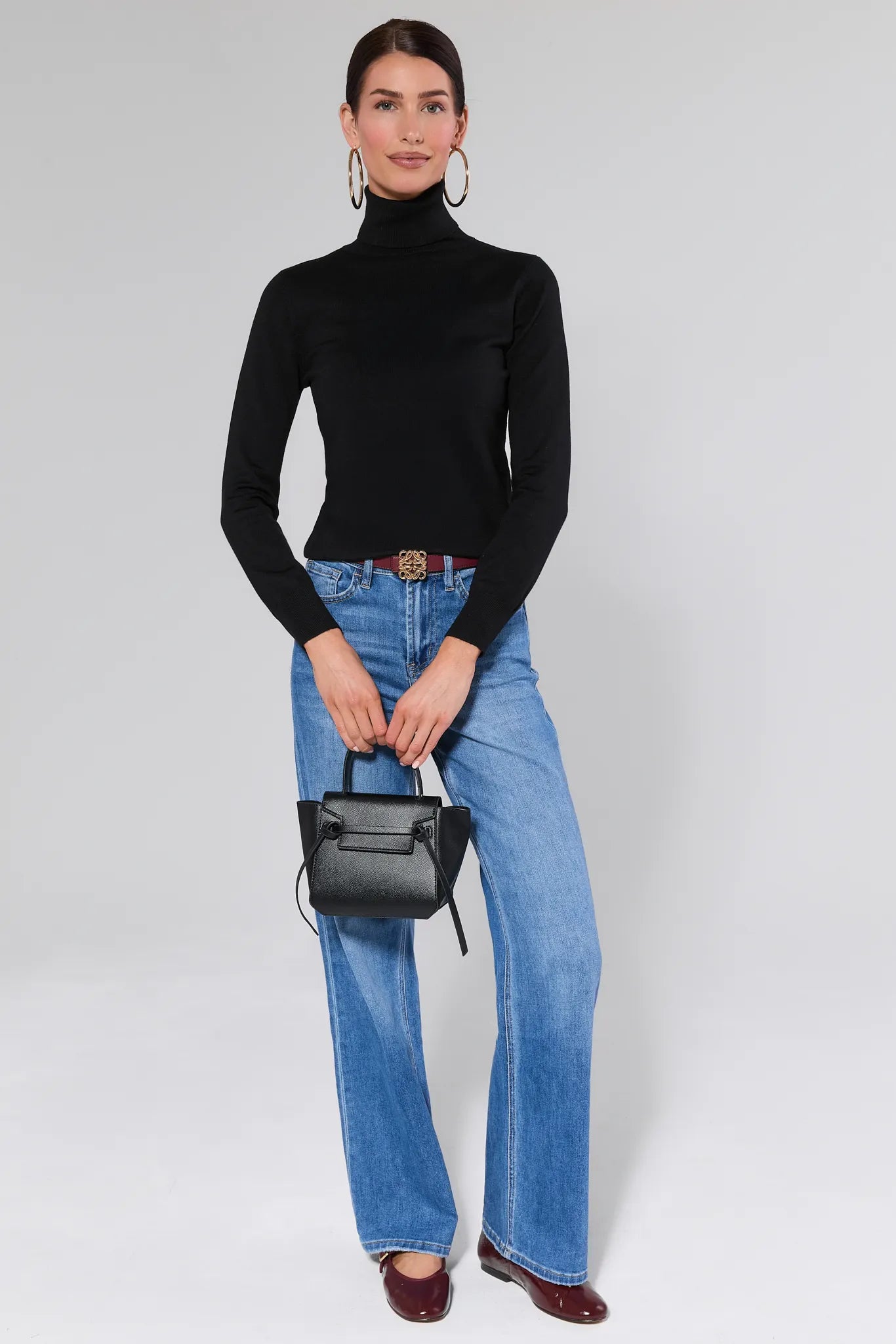 Woman wearing a Andrea Black Turtleneck Top and blue jeans against a plain background