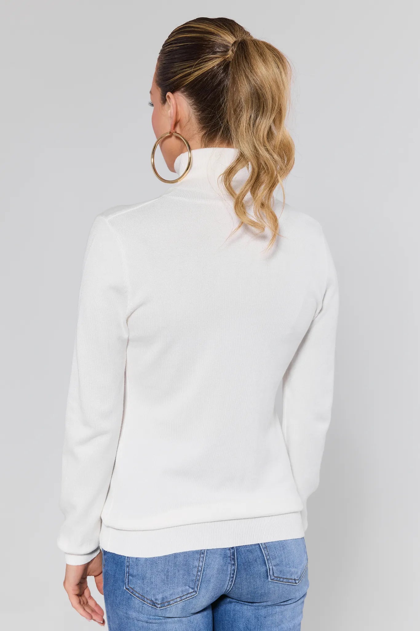 Woman wearing a Andrea Ivory Turtleneck Top sweater with gold hoop earrings on a plain background