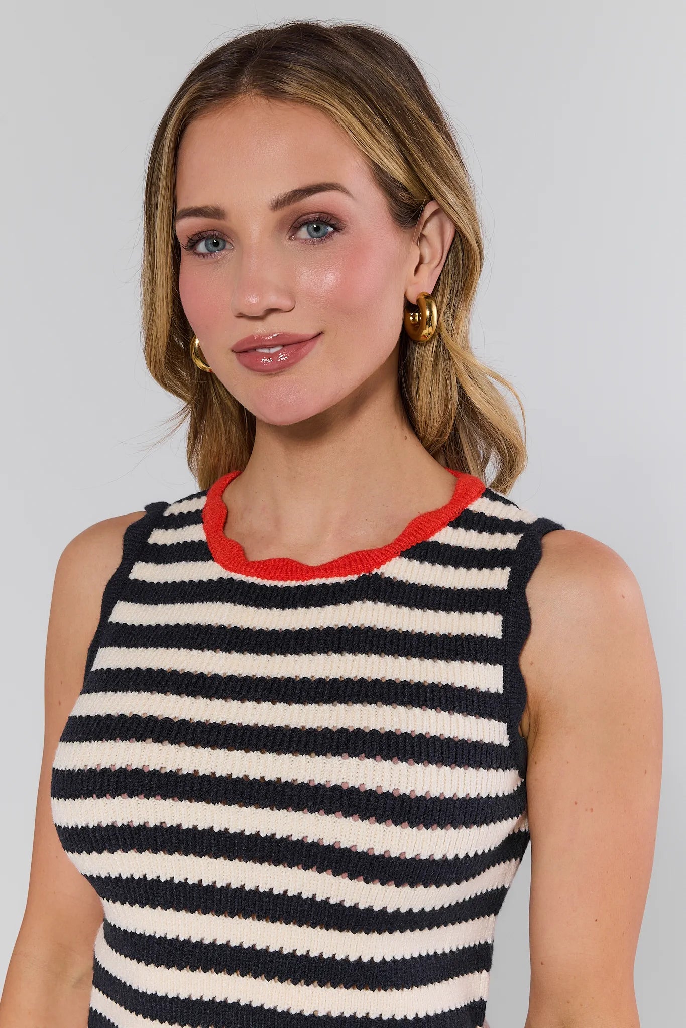 Woman wearing a black and white striped sleeveless top with red trim against a plain background