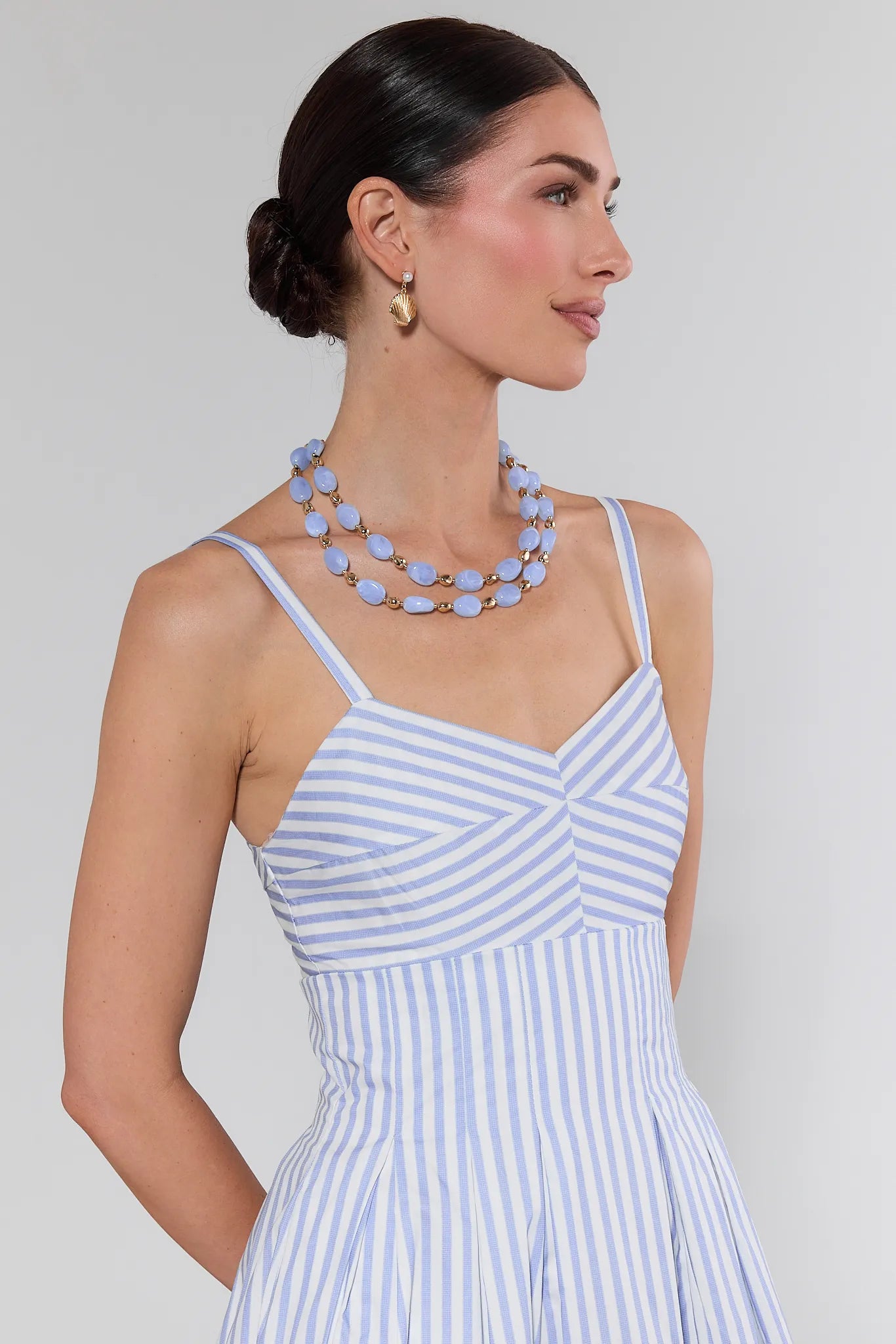 Woman wearing a blue and white striped dress with a necklace against a gray background