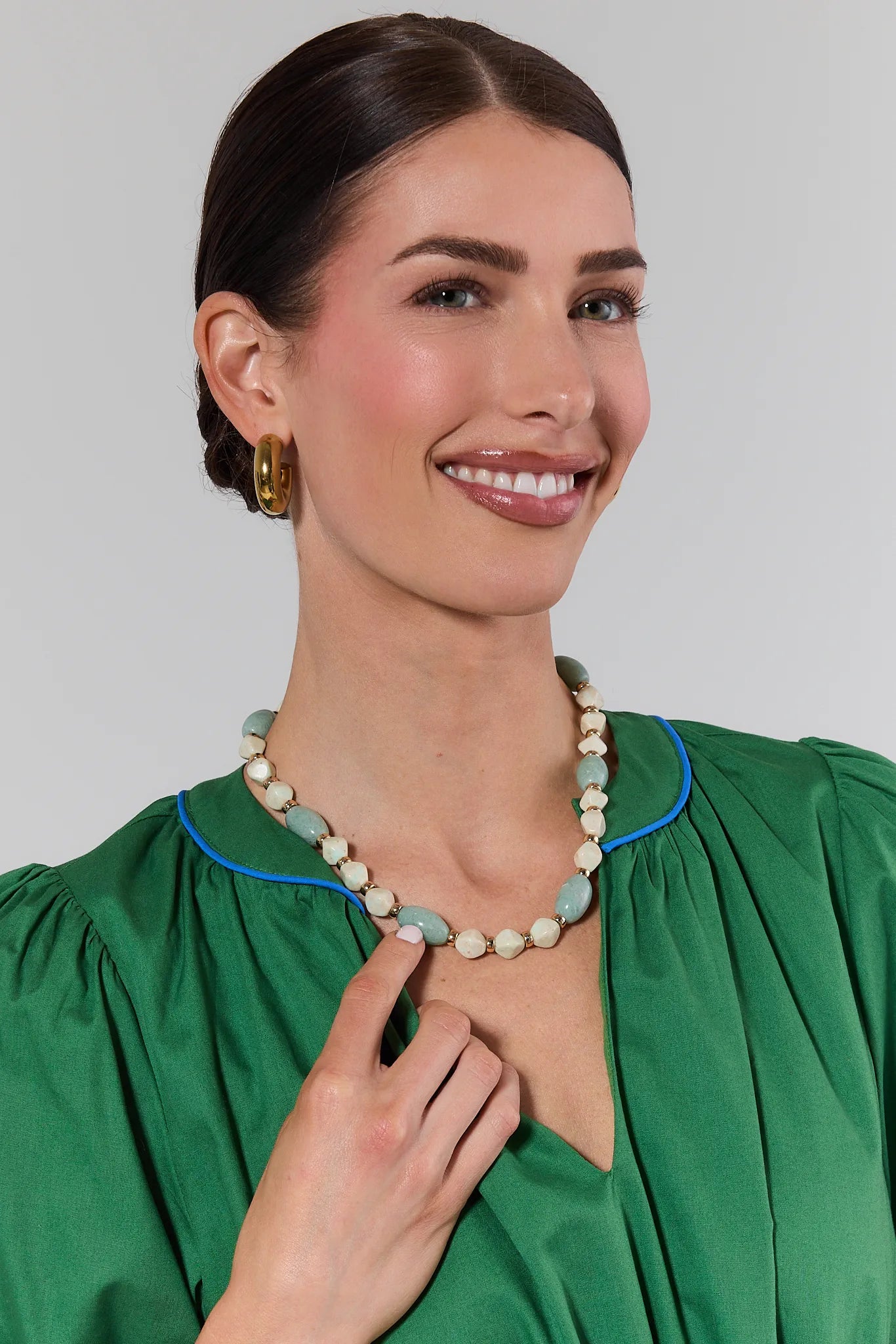 Woman wearing a green dress and necklace against a plain background