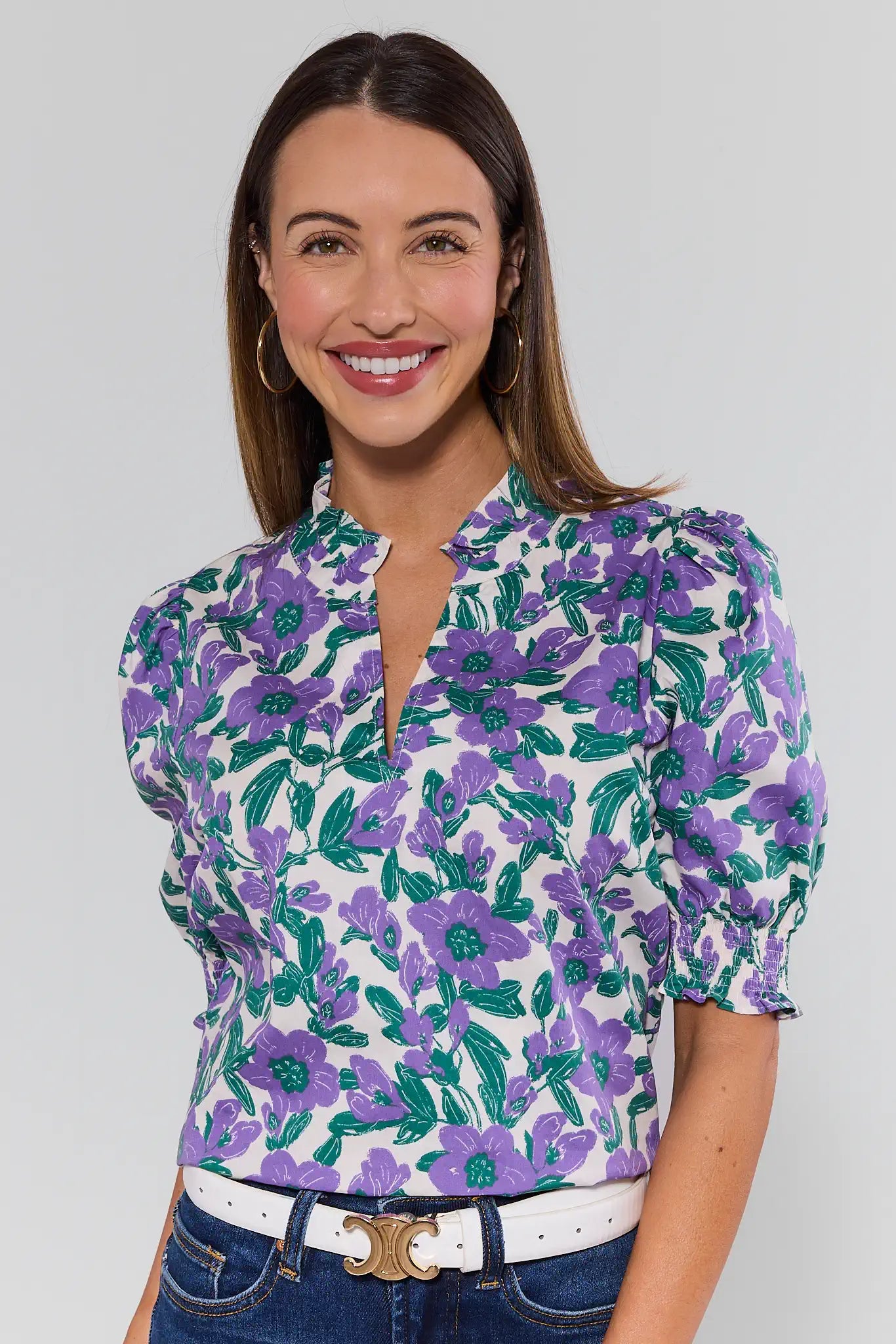 Woman wearing a floral blouse with purple and green flowers on a plain background